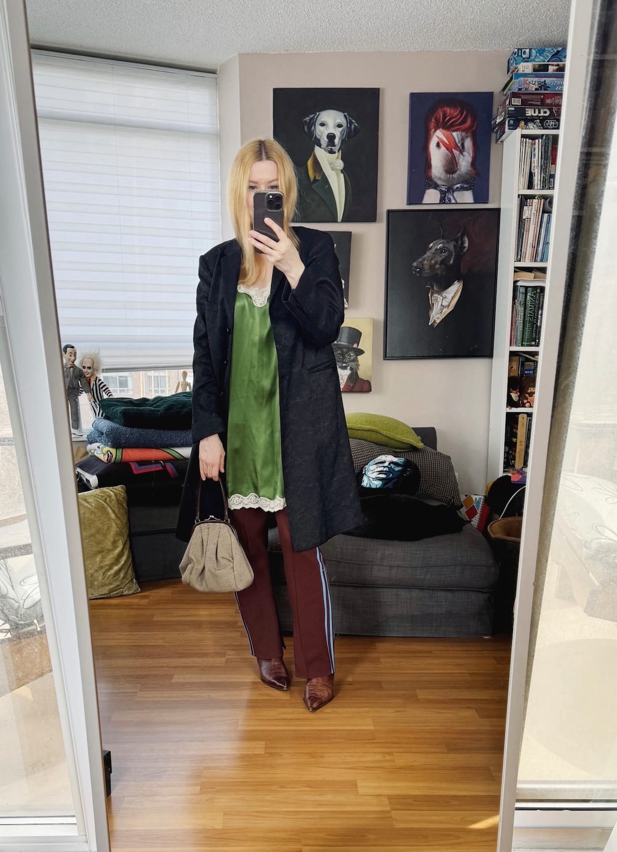Sara of livelovesara is standing in front of a mirror taking a photo of her outfit. She is wearing a green dress over brown adidas pants, vintage boots, a mid length menswear inpsired coat, and a Miu Miu kisslock bag from 2000.