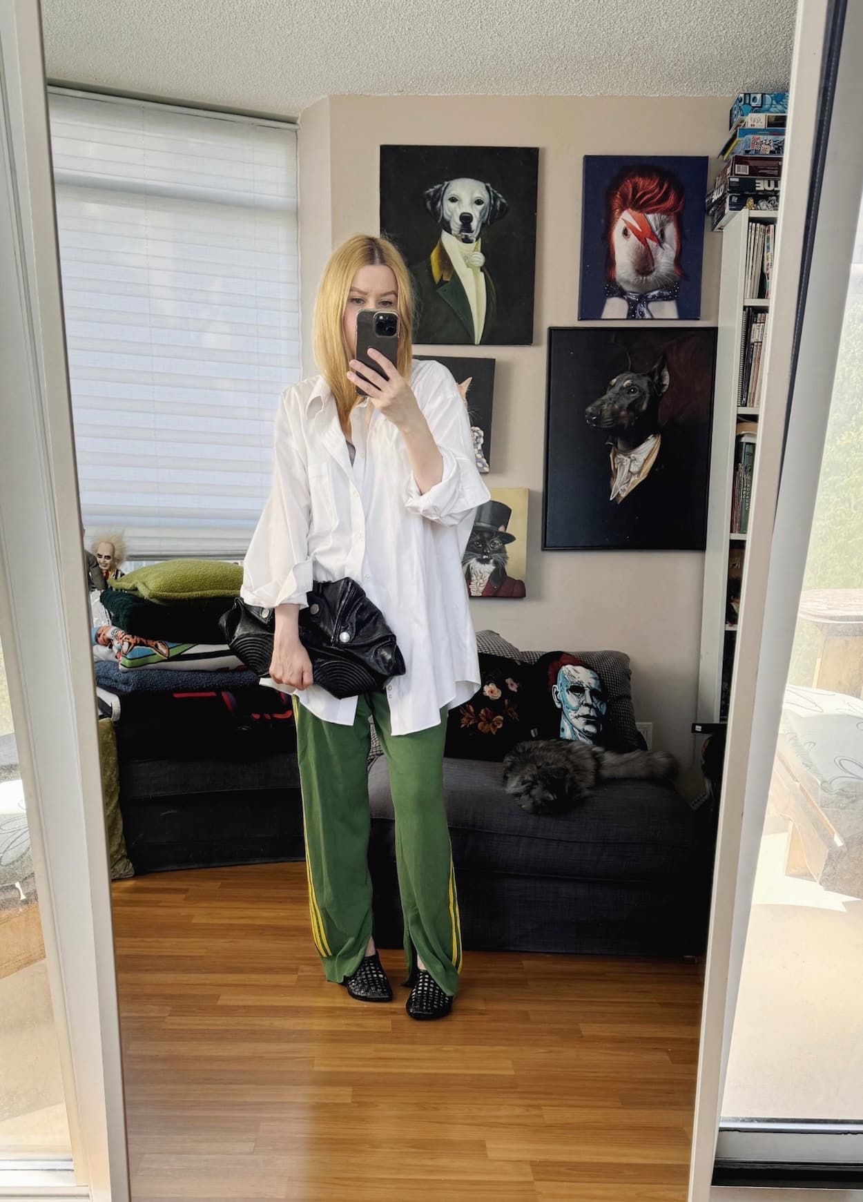 Sara of livelovesara is standing in front of a mirror taking a photo of her outfit. She is wearing a white button up with green Adidas X Wales Bonner track pants, leather mesh flats, and an Alexander McQueen de manta clutch.