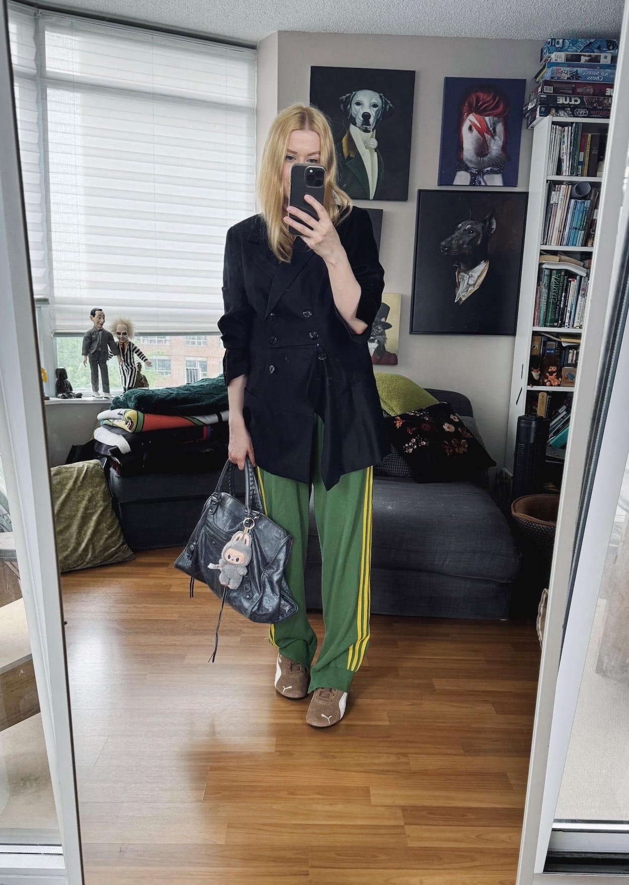 Sara of livelovesara is standing in front of a mirror taking a photo of her outfit. She is wearing a vintgae blazer, green adidas track pants, puma speedcats, and a grey balenciaga work bag.