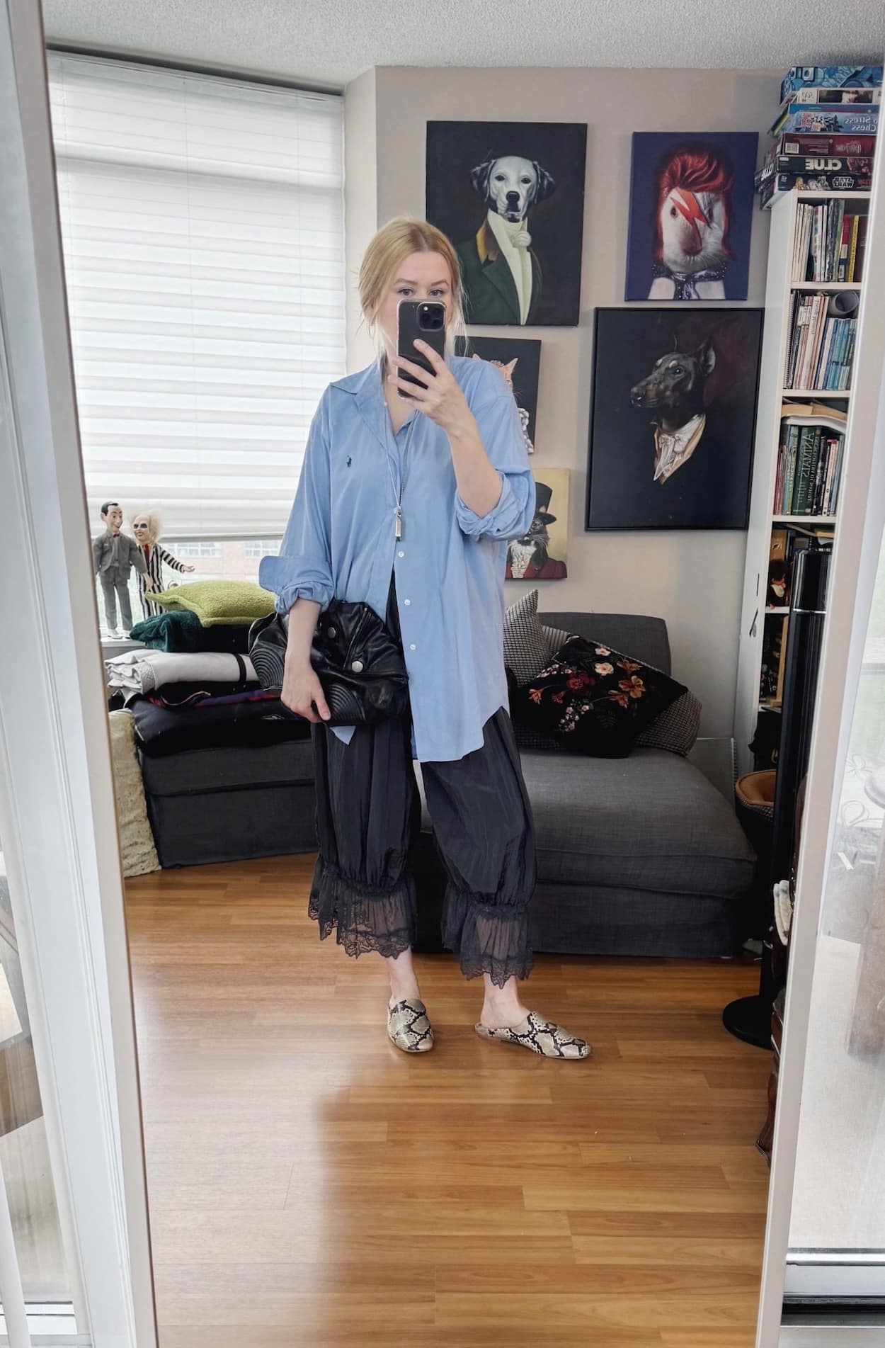 Sara of livelovesara is standing in front of a mirror taking a photo of her outfit. She is wearing a blue button up, free people bloomers, snake print mules, and an alexander mcqueen clutch.