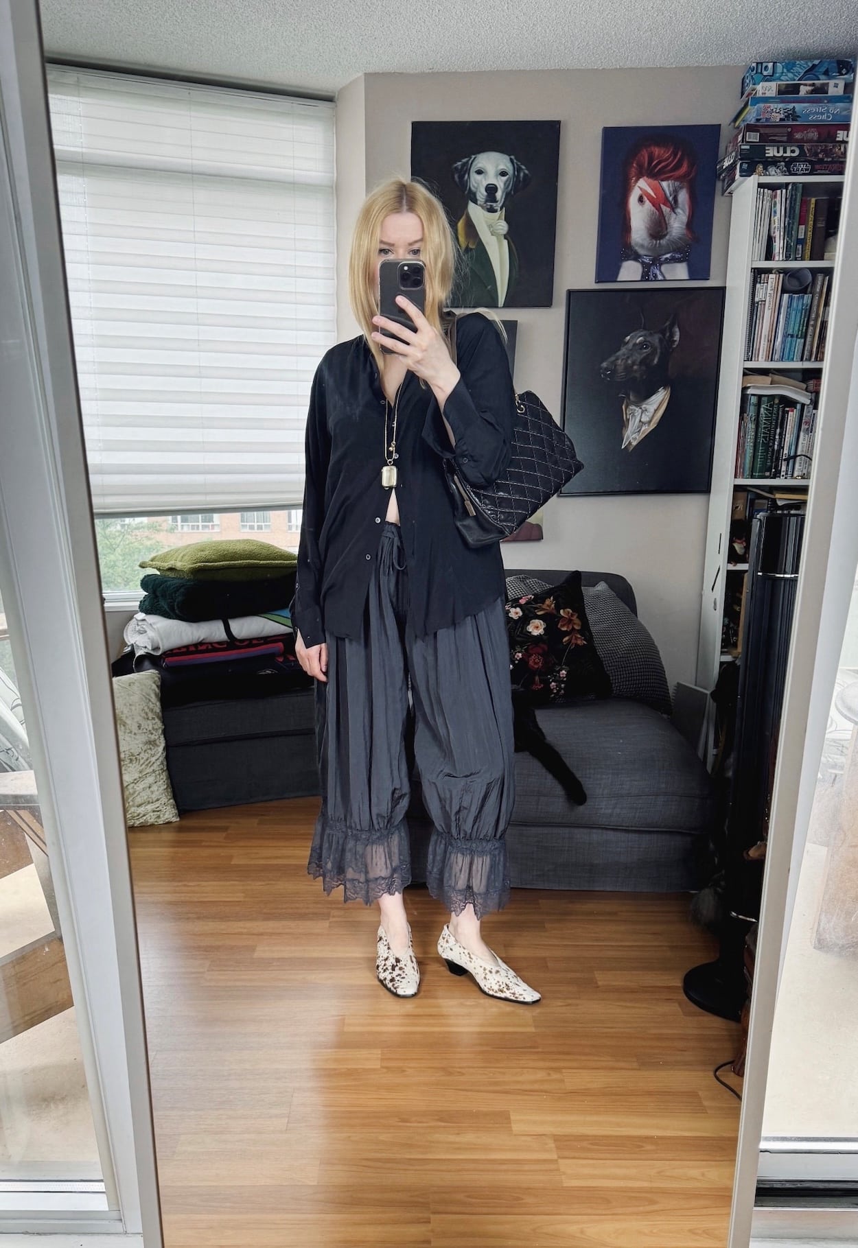Sara of livelovesara is standing in front of a mirror taking a photo of her outfit. She is wearing a black silk blouse with bloomers, an antique necklace, heels, and a vintage chanel bag.