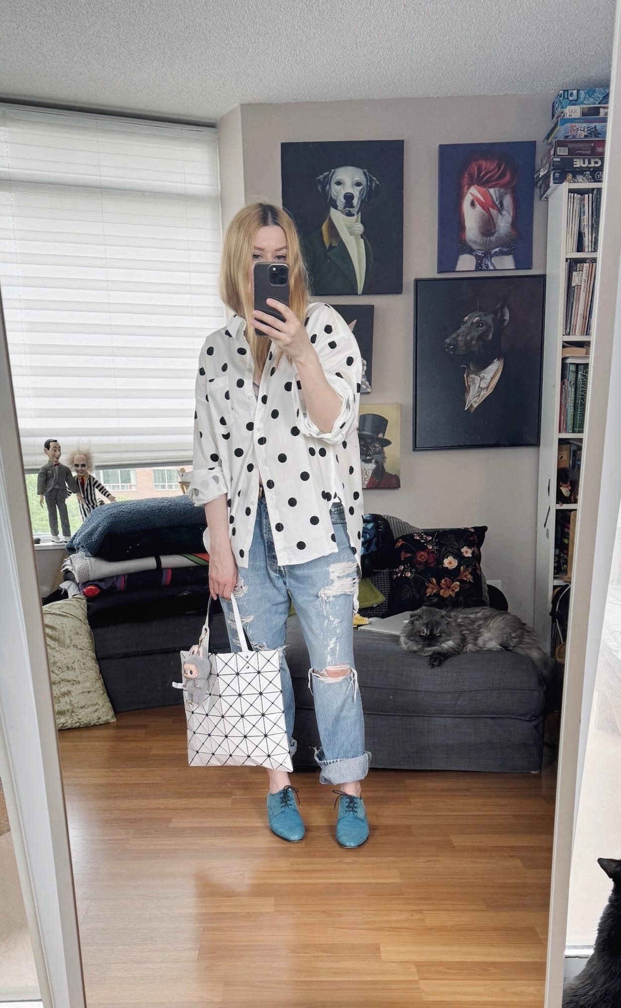 Sara of livelovesara is standing in front of a mirror taking a photo of her outfit. She is wearing a polka dot button up, distressed vintage lecis, blue oxfords, and an Issey Miyake bao bao bag.
