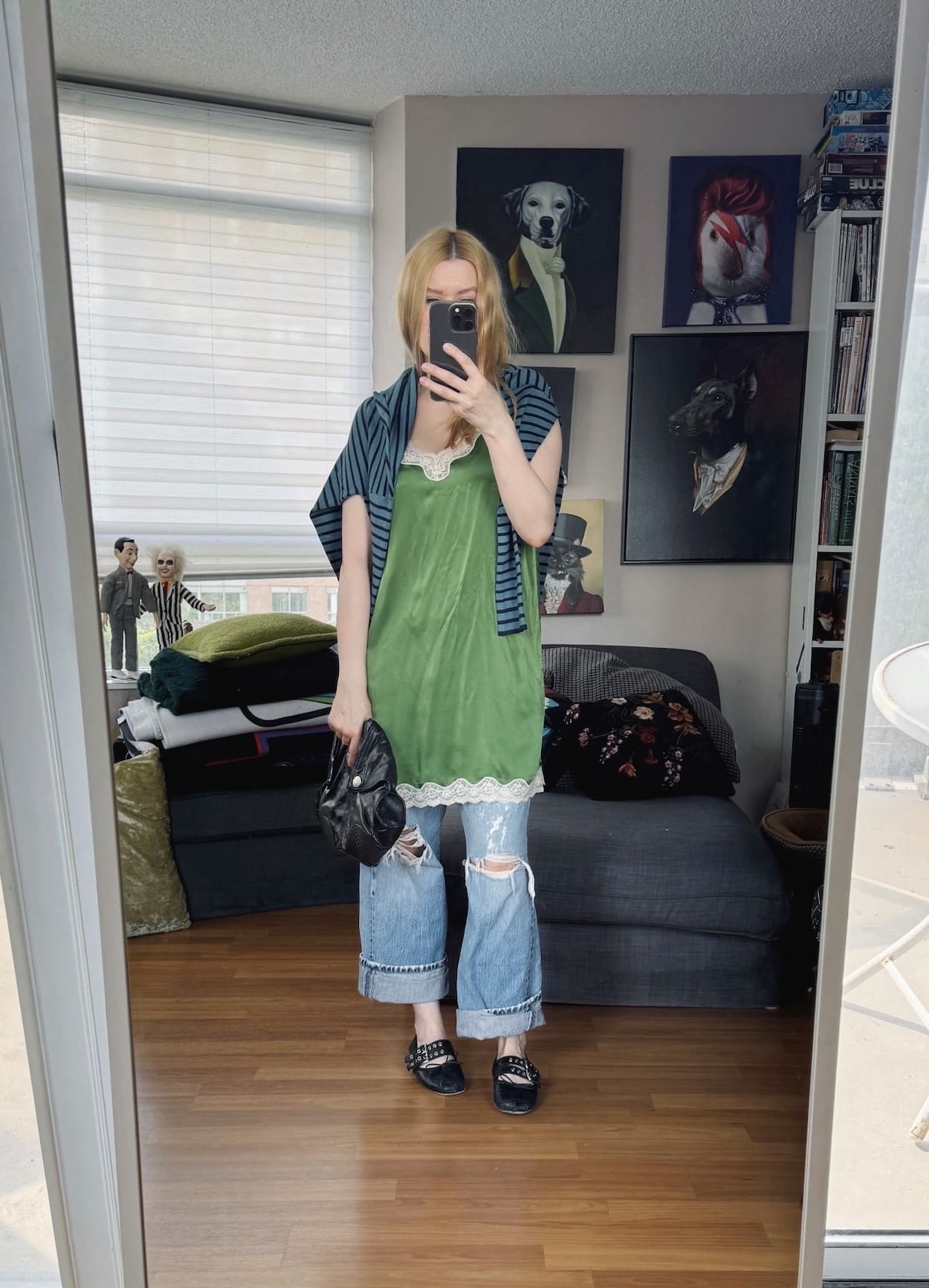Sara of livelovesara is standing in front of a mirror taking a photo of her outfit. She is wearing a green short slip dress over distressed vintage Levis, a striped sweater around her shoulders, black ballet flats, and an Alexander McQueen clutch.
