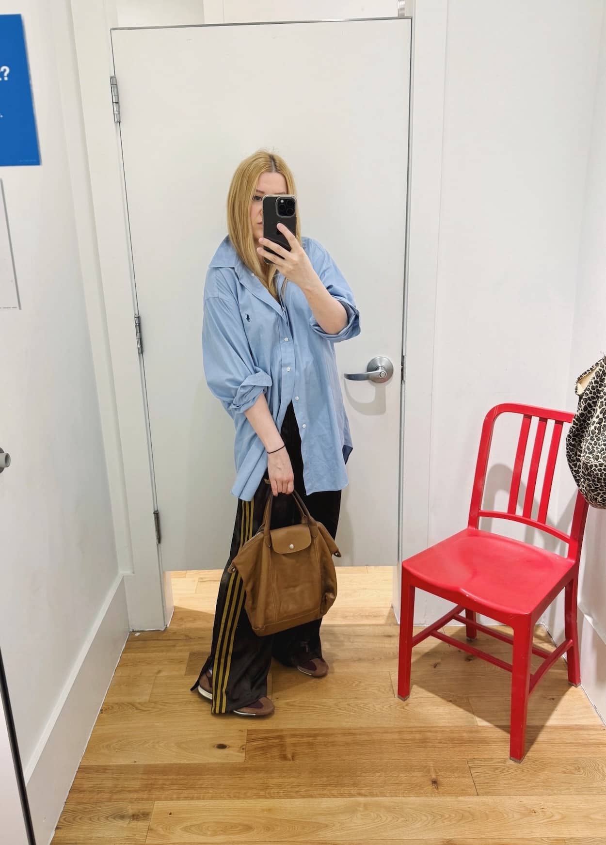 Sara of livelovesara is standing in front of a mirror taking a photo of her outfit. She is wearing a blue button up with brown adidas track pants, brown adidas SL 72 sneakers, and a tan Longchamp Le Pliage Cuir bag. 