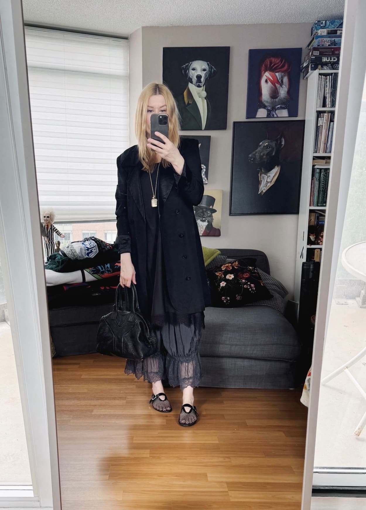 Sara of livelovesara is standing in front of a mirror taking a photo of her outfit. She is wearing a tunic shirt over black bloomer pants, a long black tuxedo jacket, mesh flats, a black bag, and a antique vesta necklace.