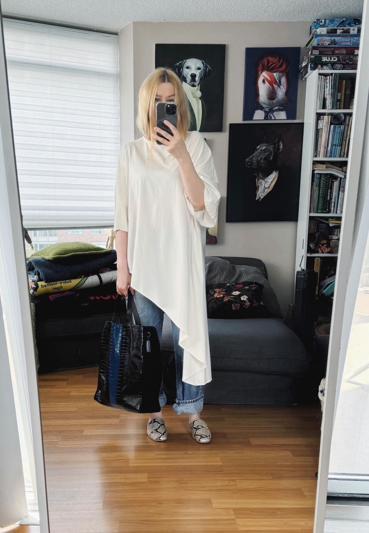 Sara of livelovesara is standing in front of a mirror taking a photo of her outfit. She is wearing an asymmetrical t-shirt with vintage Levis, mules, and is carrying a tote.
