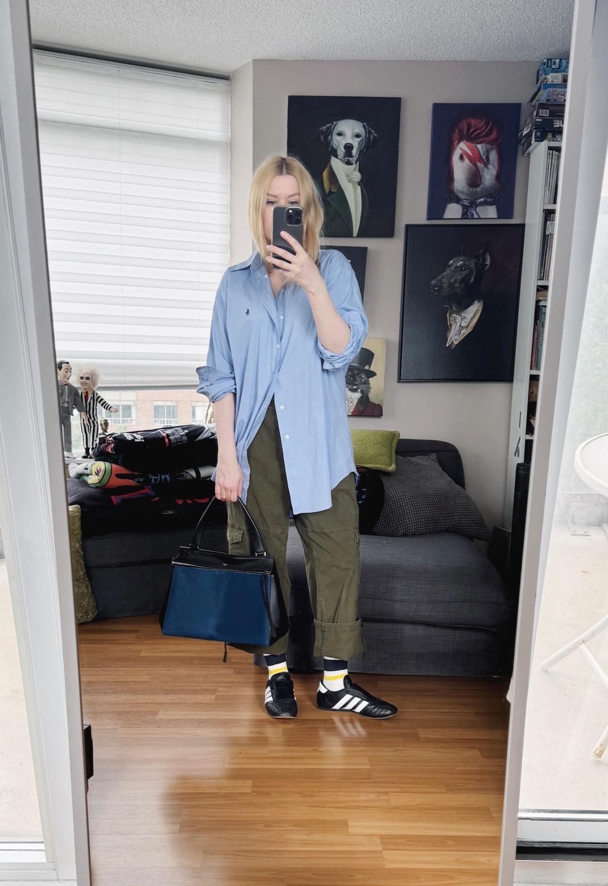 Sara of livelovesara is standing in front of a mirror taking a photo of her outfit. She is wearing a blue button up over cargo pants, striped socks, adidas sneakers, and a blue Celine bag.