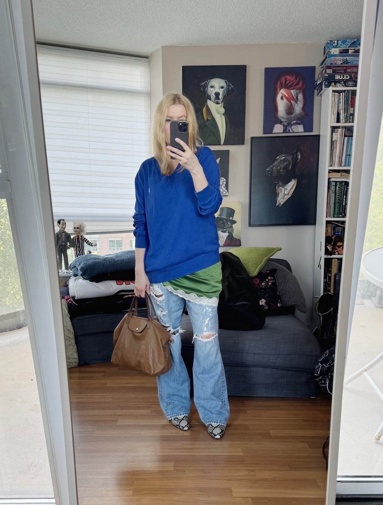 Sara of livelovesara is standing in front of a mirror taking a photo of her outfit. She is wearing a cobalt blue sweater over a green camisole, distressed vintage Levi's, snake print boots, and a brown handbag.