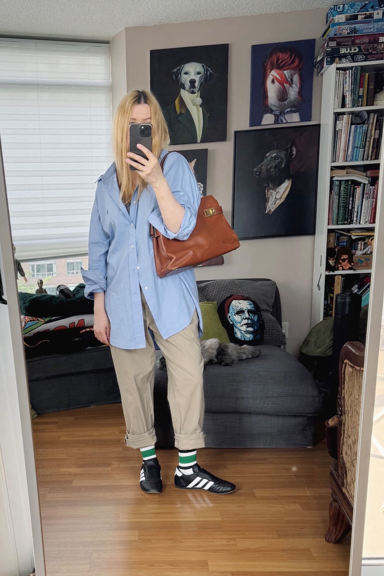 Sara of livelovesara is standing in front of a mirror taking a photo of her outfit. She is wearing a blue button up, khakis, striped socks, black sneakers, and a Ferragamo bag.