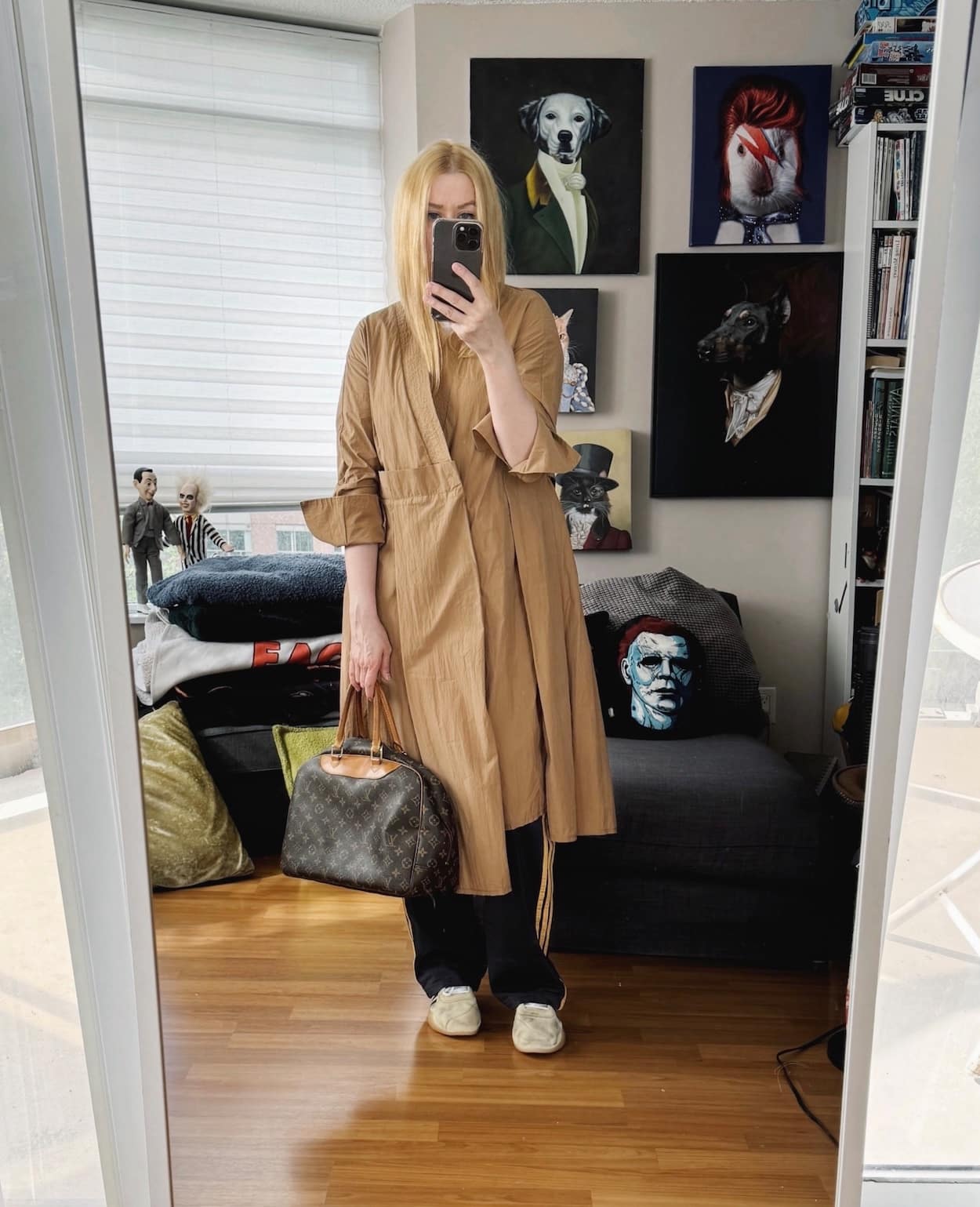 Sara of livelovesara is standing in front of a mirror taking a photo of her outfit. She is wearing a vintage trench with a white tee, Adidas track pants, Adidas x song of the mute sneakers, and a vintage bag.