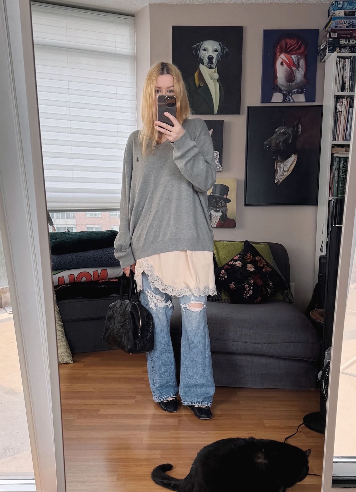 Sara of livelovesara is standing in front of a mirror taking a photo of her outfit. She is wearing a grey sweater over a slip shirt, vintage levis, ballet flats, and a ysl easy bag.