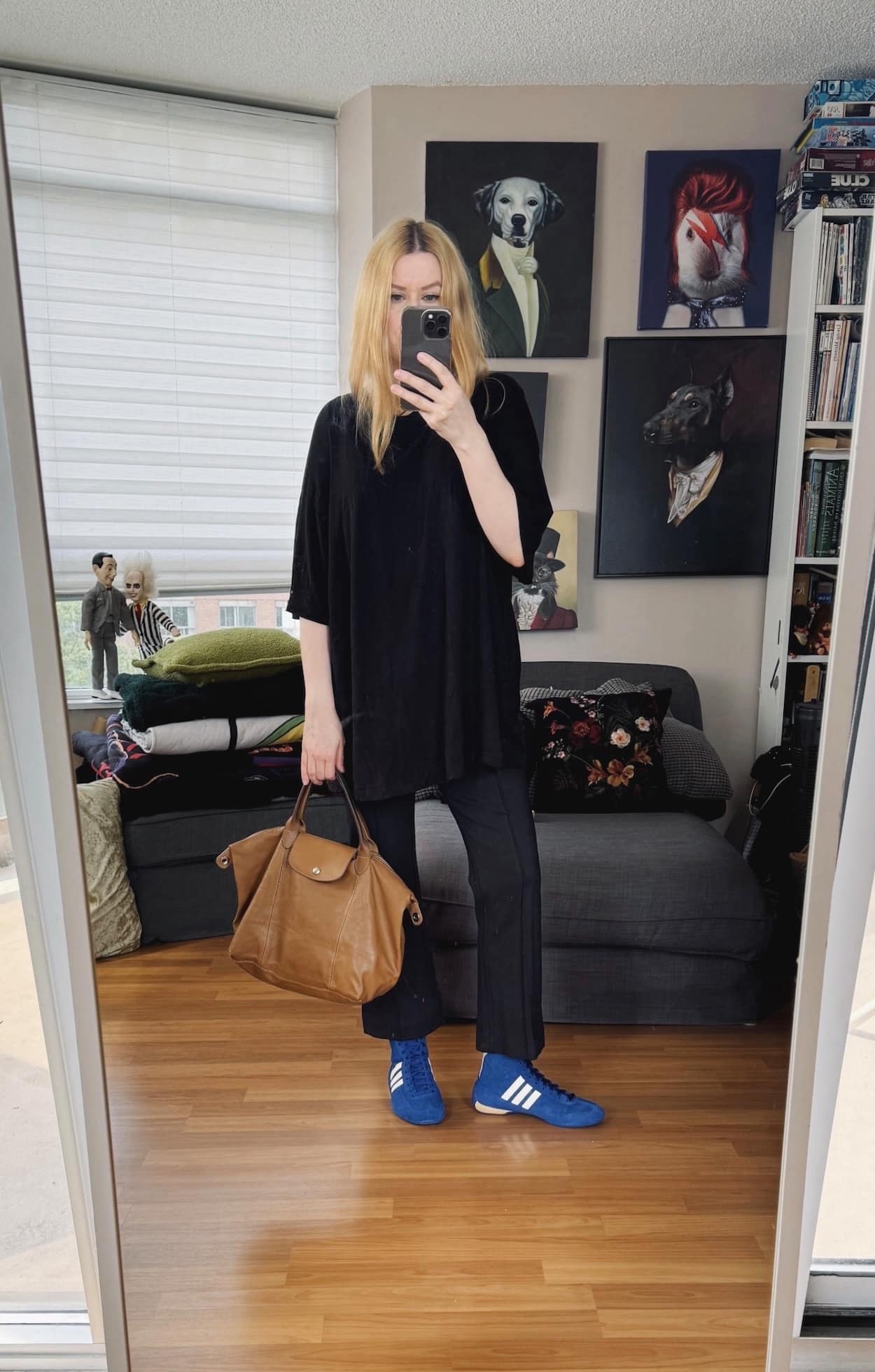 Sara of livelovesara is standing in front of a mirror taking a photo of her outfit. She is wearing a black tee, black kick flares, blue sneakers, and a longchamp bag.