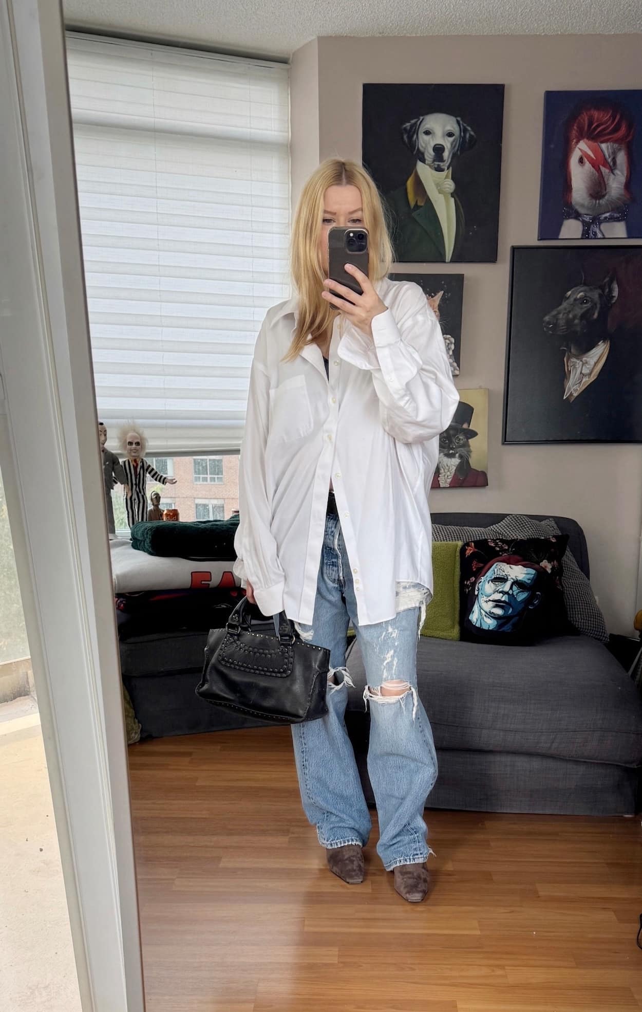 Sara of livelovesara is standing in front of a mirror taking a photo of her outfit. She is wearing a white button up with vintage levis, brown boots, and is carrying a celine boogie bag.