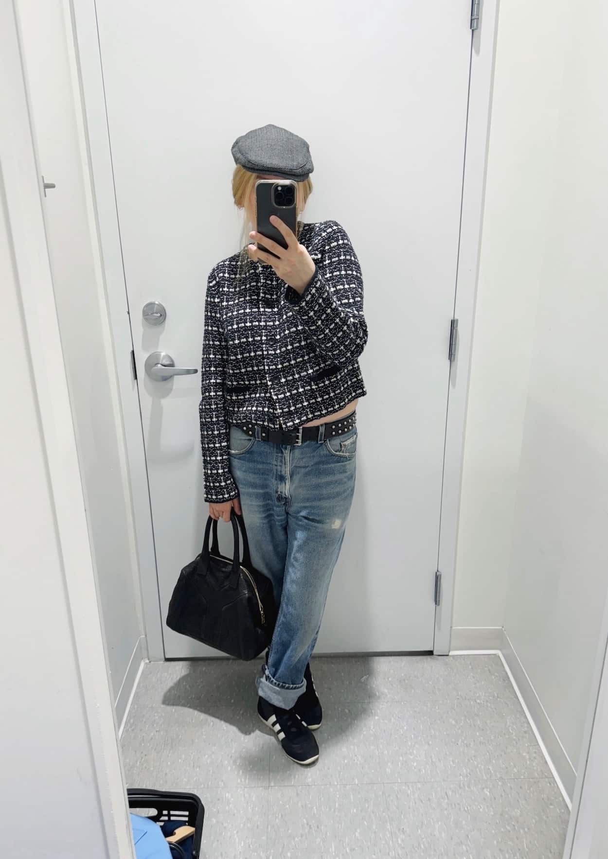 Sara of livelovesara is standing in front of a mirror taking a photo of her outfit. She is wearing a tweed cropped jacket with vintage levis, a studded belt, high sneakers, a driving cap, and a ysl easy bag.