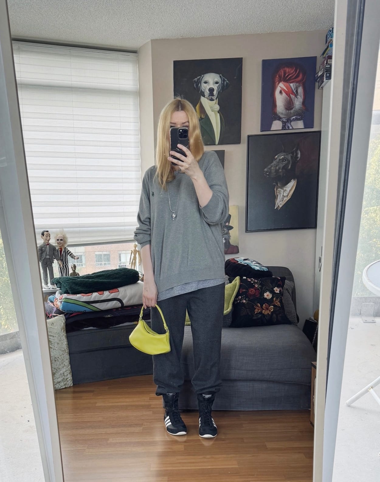 Sara of livelovesara is standing in front of a mirror taking a photo of her outfit. She is wearing a a grey sweater over a t-shirt, grey trousers, high sneakers, a cat pendant, and a neon bag.