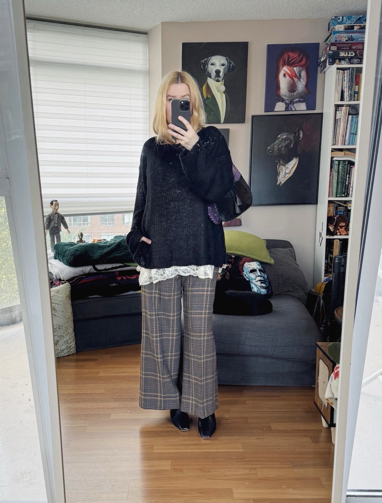Sara of livelovesara is standing in front of a mirror taking a photo of her outfit. She is wearing an open weave sweater over a camisole, plaid trousers, mules, and a vintage bag.