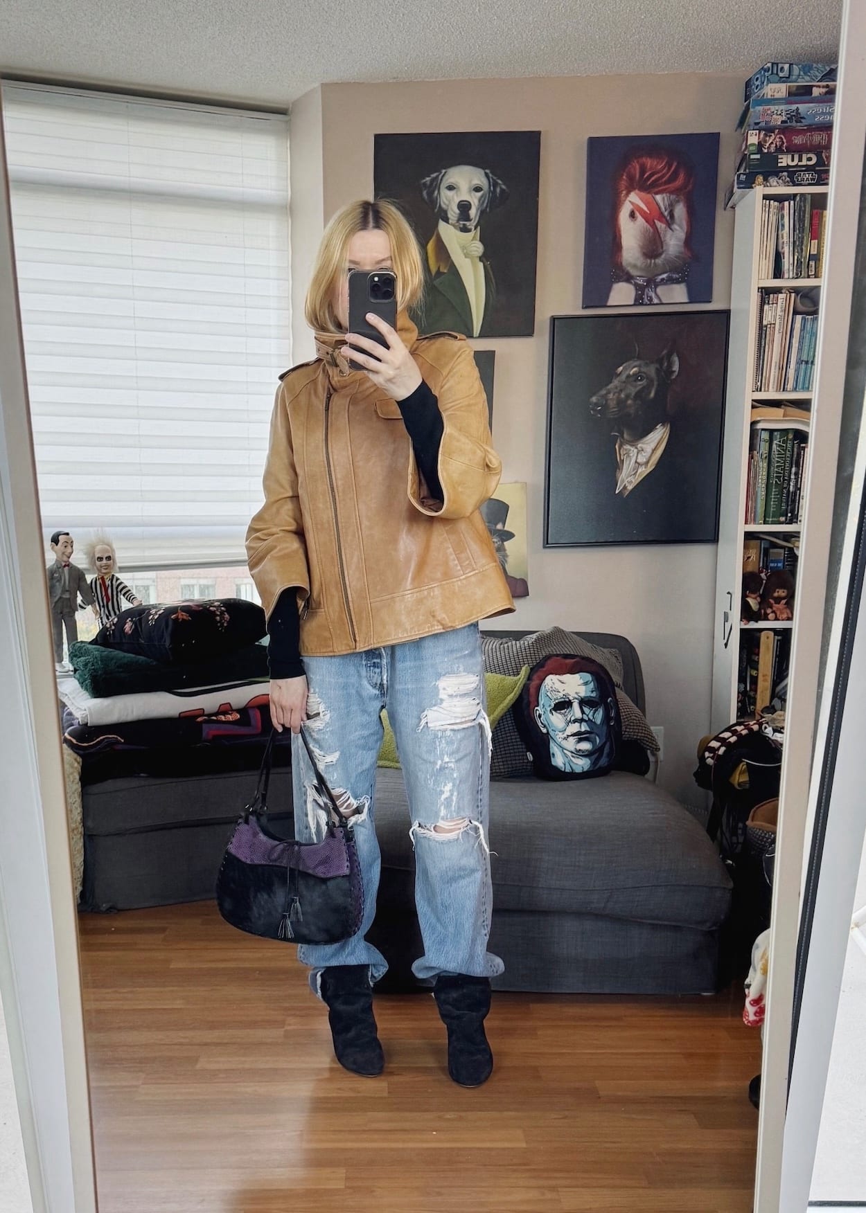 Sara of livelovesara is standing in front of a mirror taking a photo of her outfit. She is wearing a black turtleneck, with a funnel neck leather jacket, vintage levis, black slouch boots, and a vintage bag.