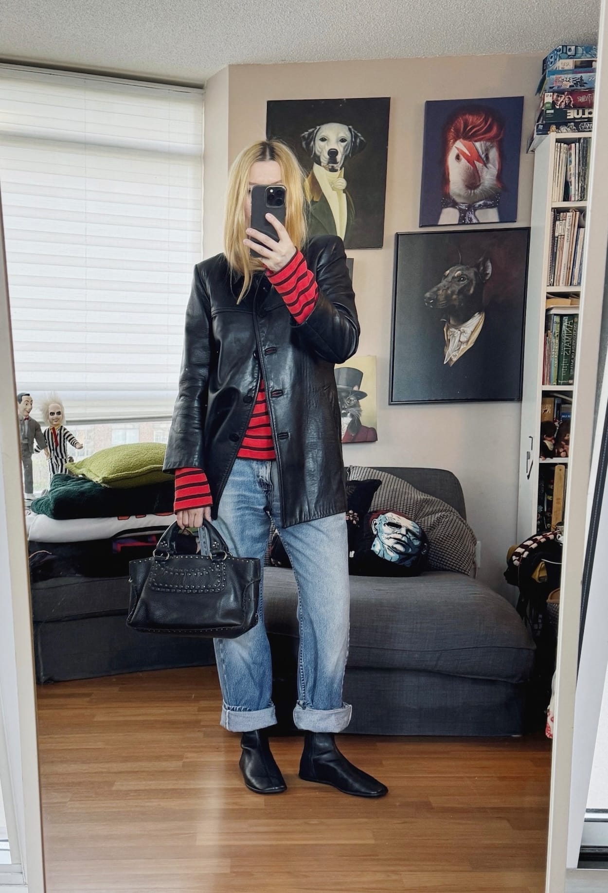 Sara of livelovesara is standing in front of a mirror taking a photo of her outfit. She is wearing a red striped sweater under a leather jacket, vintage levis, black flat boots, and is carrying a celine boogie bag.