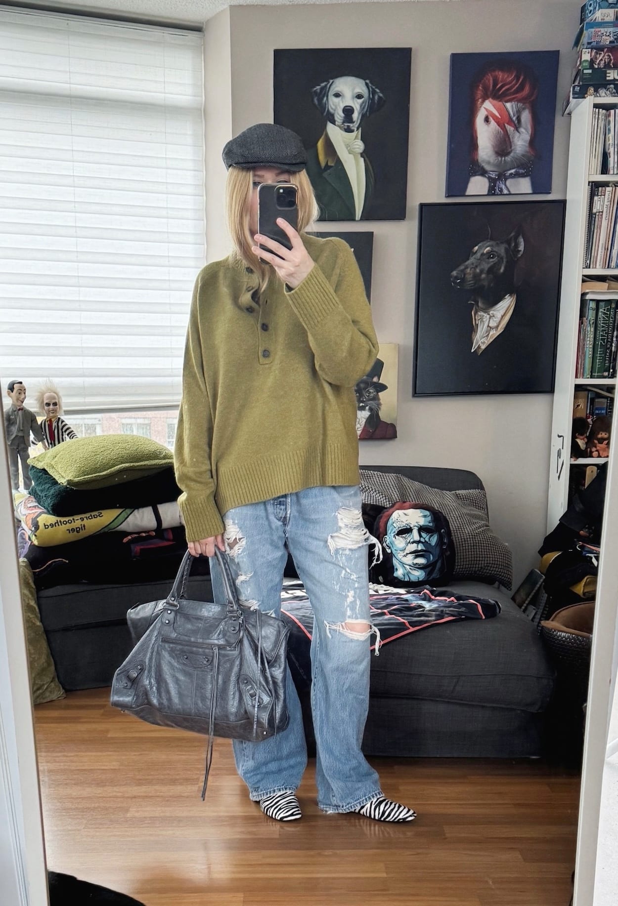 Sara of livelovesara is standing in front of a mirror taking a photo of her outfit. She is wearing a green sweater with vintage levis, zebra print loafers, a herringbone cap, and a Balenciaga bag.