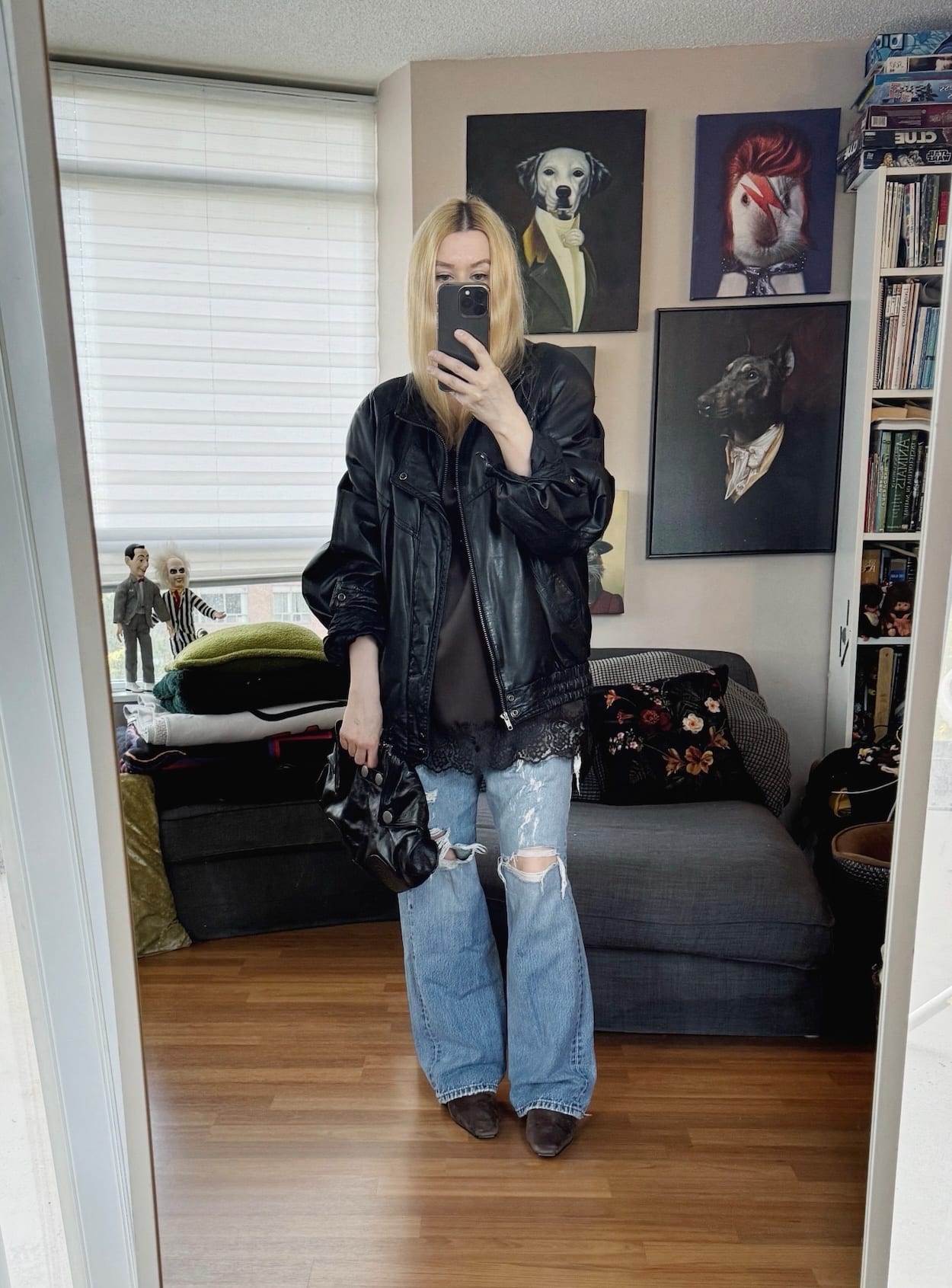 Sara of livelovesara is standing in front of a mirror taking a photo of her outfit. She is wearing a long camisole over vintage Levis, a vintage bomber jacket, brown boots, and is carrying an Alexander McQueen clutch.