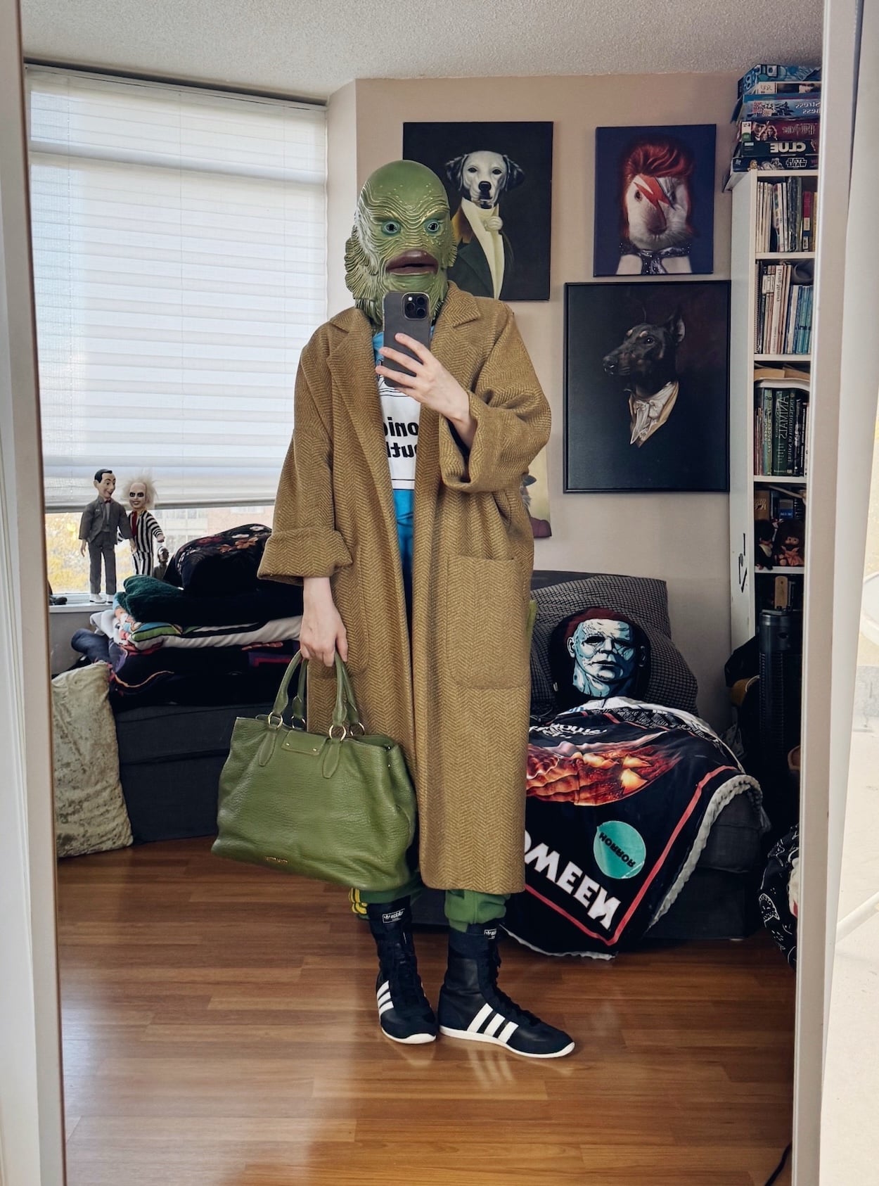 Sara of livelovesara is standing in front of a mirror taking a photo of her outfit. She is wearing a sonic youth tee, horses atelier alchemical coat, green adidas track pants, black adidas wrestling sneakers, a green tote, and is wearing a creature from the black lagoon halloween mask.