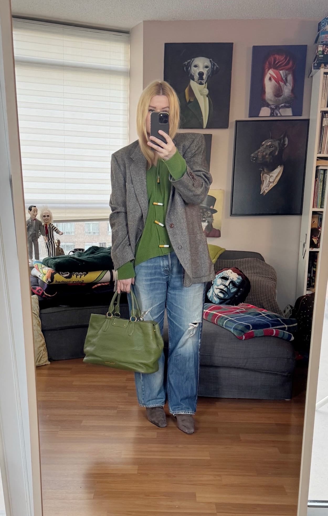 Sara of livelovesara is standing in front of a mirror taking a photo of her outfit. She is wearing a green cardigan with cigarette shaped buttons under a tweed blazer, vintage Levi's brown boots, and is carrying a green tote.
