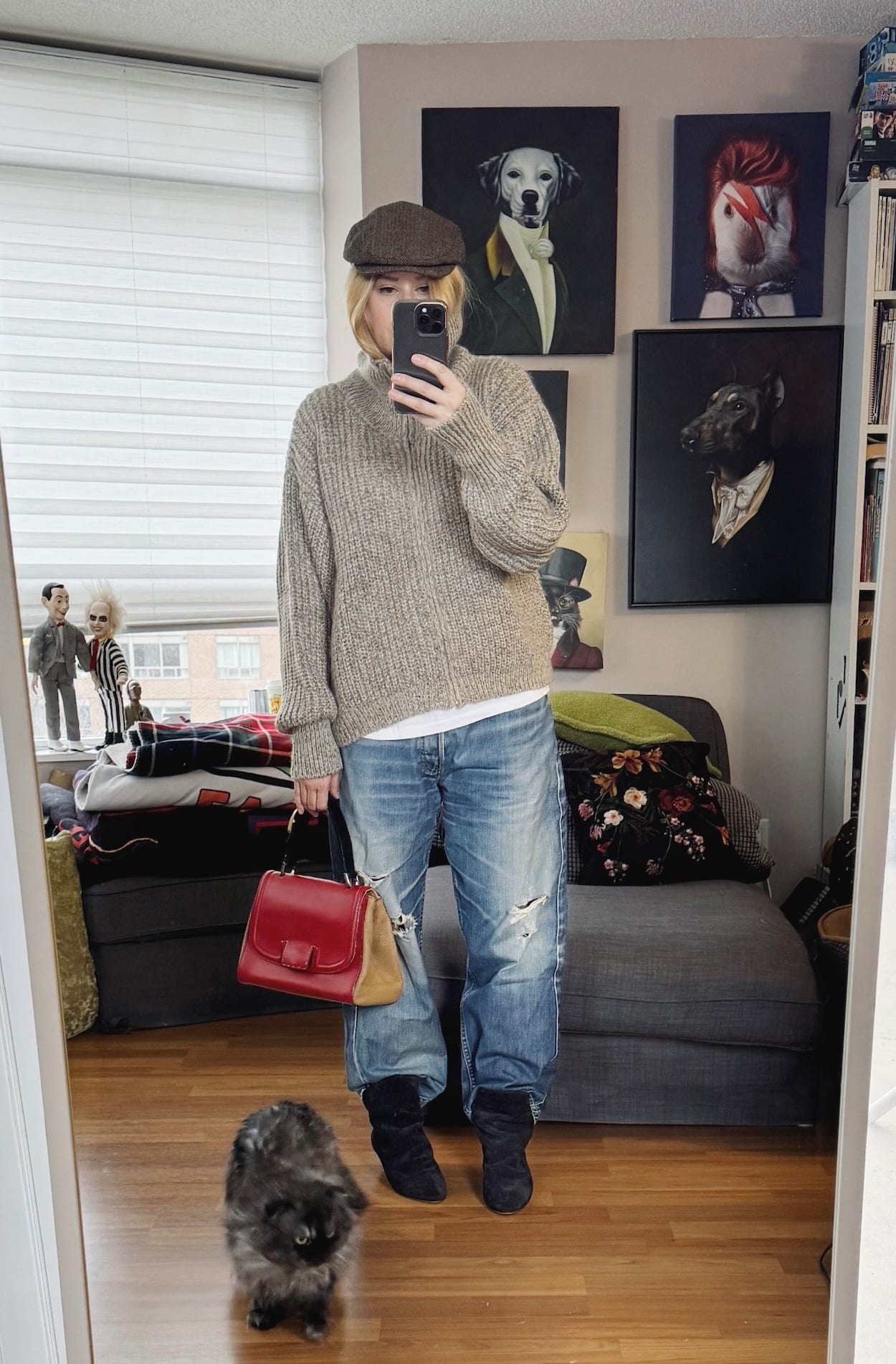 Sara of livelovesara is standing in front of a mirror taking a photo of her outfit. She is wearing a white t-shirt under a cowl neck sweater, vintage levis, slouchy boots, a flat cap, and is carrying a fendi bag.