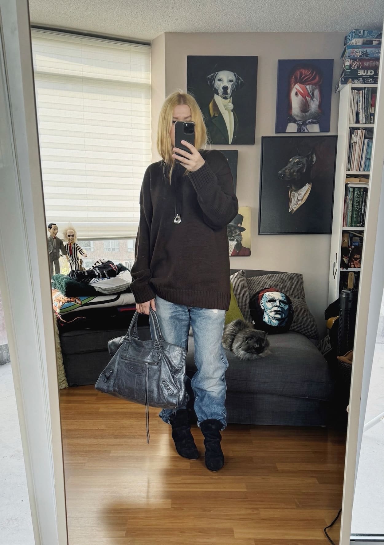 Sara of livelovesara is standing in front of a mirror taking a photo of her outfit. She is wearing a brown sweater with vintage levis, slouchy boots, a pendant, and is carrying a grey Balenciaga bag.