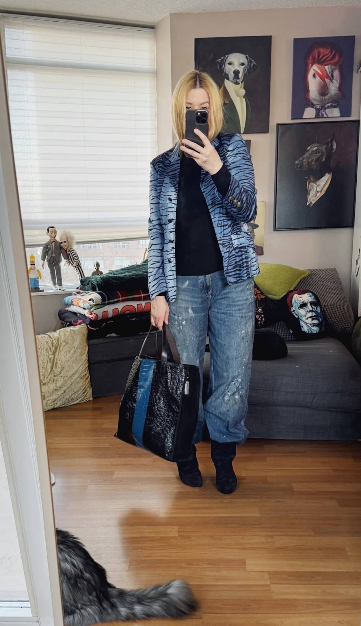 Sara of livelovesara is standing in front of a mirror taking a photo of her outfit. She is wearing a black knit turtleneck under a blue vintage tiger print blazer, paint splatter jeans, Isabel Marant slouchy boots, and a Striped bag,