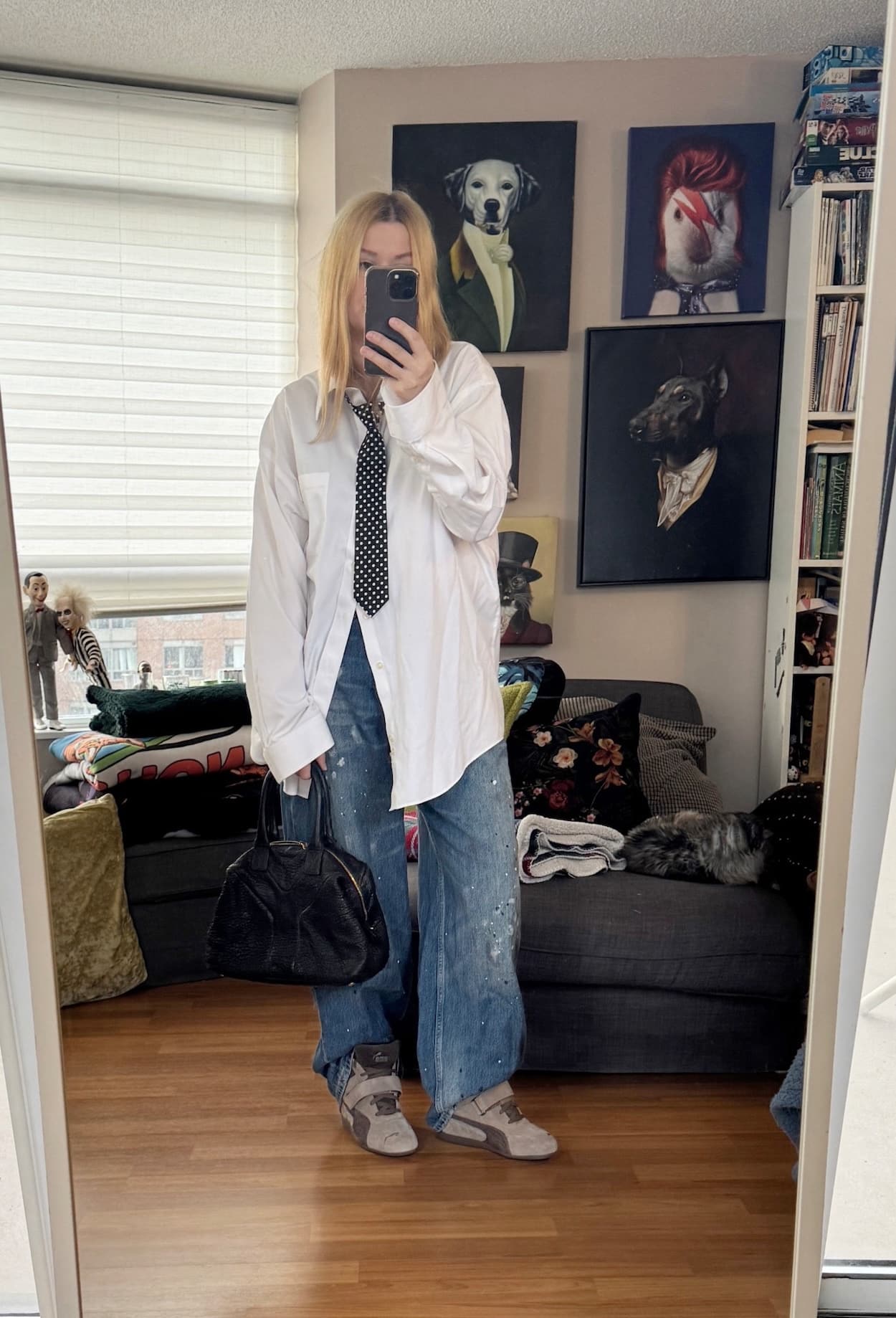 Sara of livelovesara is standing in front of a mirror taking a photo of her outfit. She is wearing an oversized white button up with a loose tie, paint splattered jeans, Puma wedge sneakers, and is carrying a ysl easy bag.