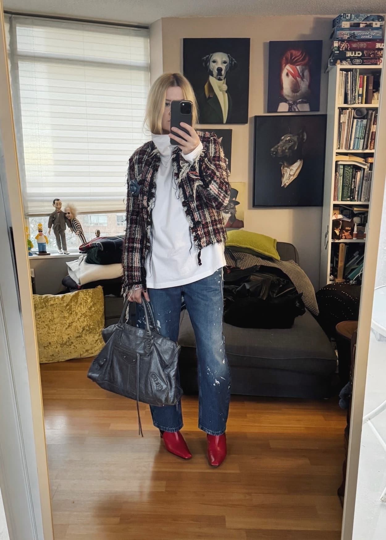 Sara of livelovesara is standing in front of a mirror taking a photo of her outfit. She is wearing a white mockneck under a vintage tweed jacket, paint splatter jeans, red boots, and a balenciaga bag.