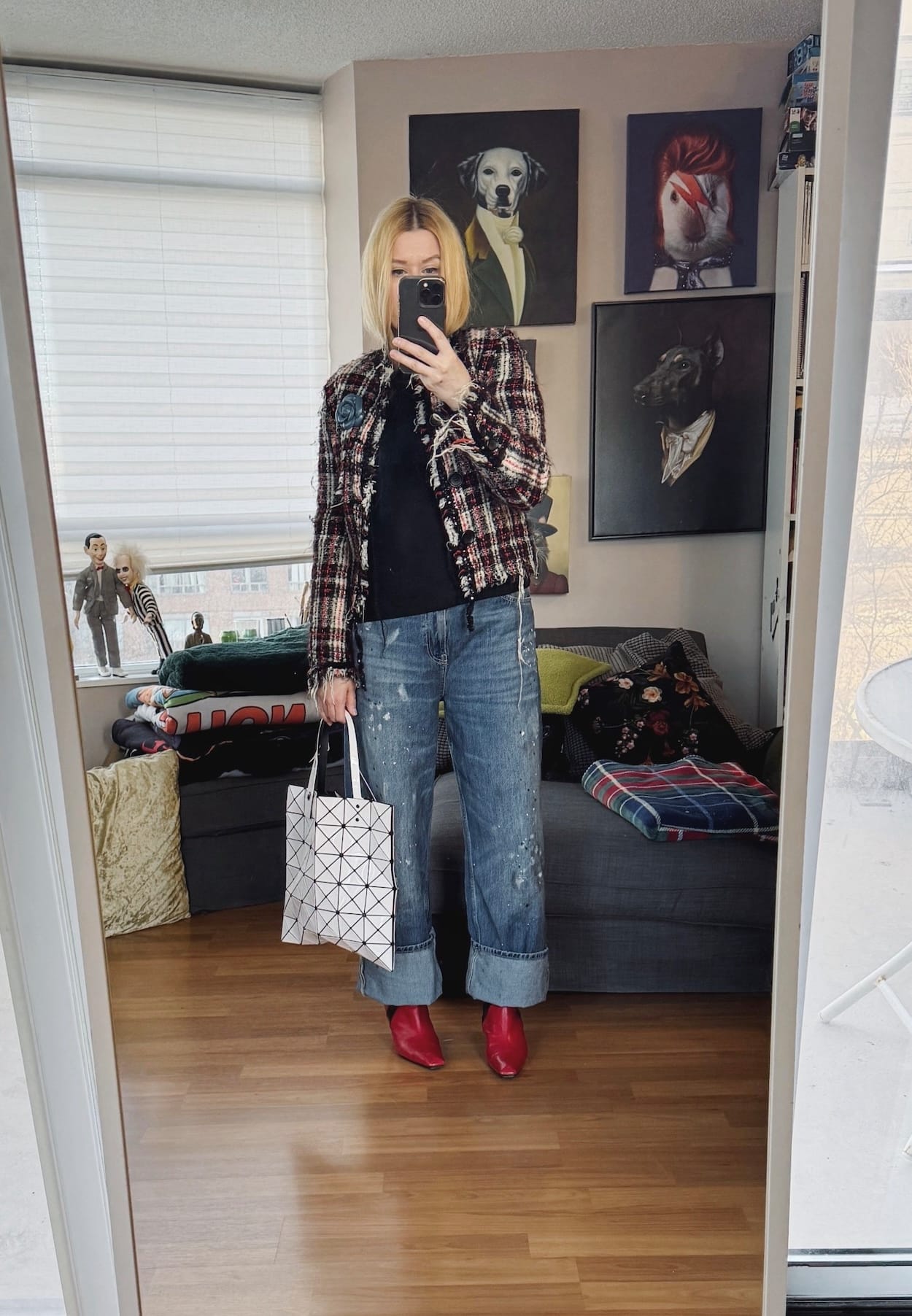 Sara of livelovesara is standing in front of a mirror taking a photo of her outfit. She is wearing a black knit turtleneck under a vintage Junya Watanabe tweed jacket, paint splattered jeans, red vintage boots, and an Issey Miyake Bao Bao bag.