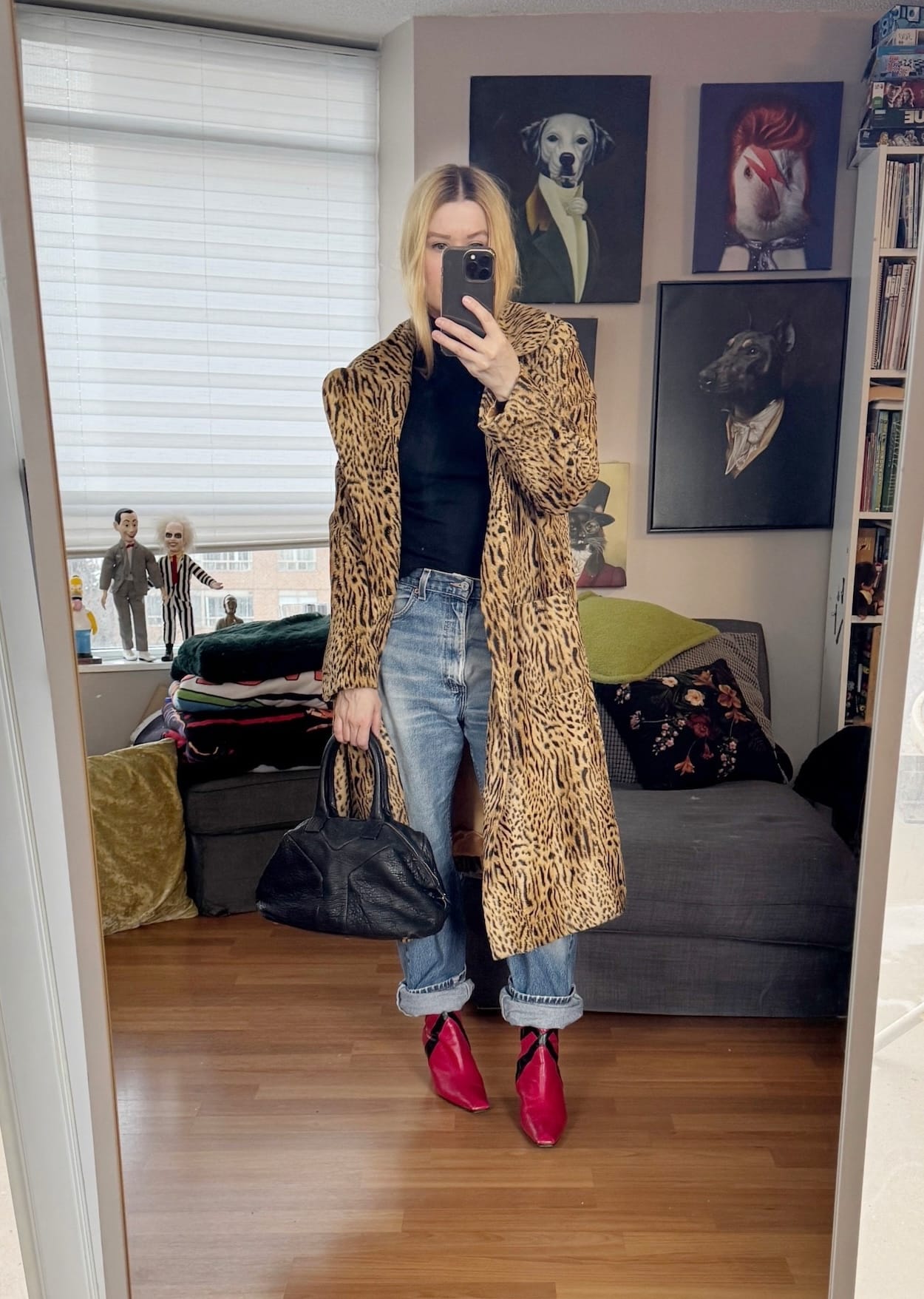 Sara of livelovesara is standing in front of a mirror taking a photo of her outfit. She is wearing a black turtleneck with vintage jeans, red vintage boots, a vintage animal print coat, and is carrying a YSL easy bag.