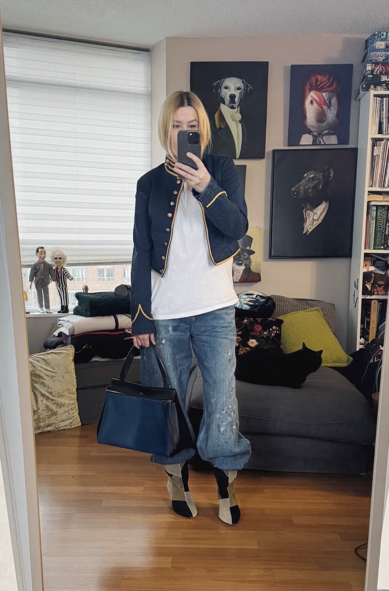 Sara of livelovesara is standing in front of a mirror taking a photo of her outfit. She is wearing a napoleon jacket over a white t-shirt, jeans, patch pattern suede boots, and a blue old celine bag.