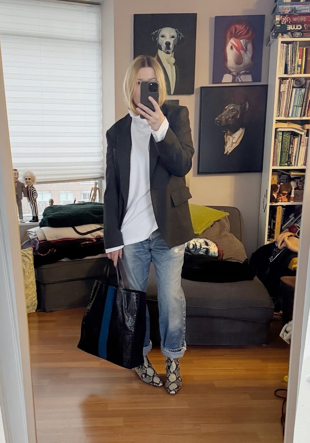Sara of livelovesara is standing in front of a mirror taking a photo of her outfit. She is wearing a white funnel neck under a grey blazer, vintage levis, snake print boots, and is carrying a striped Dries Van Noten tote.