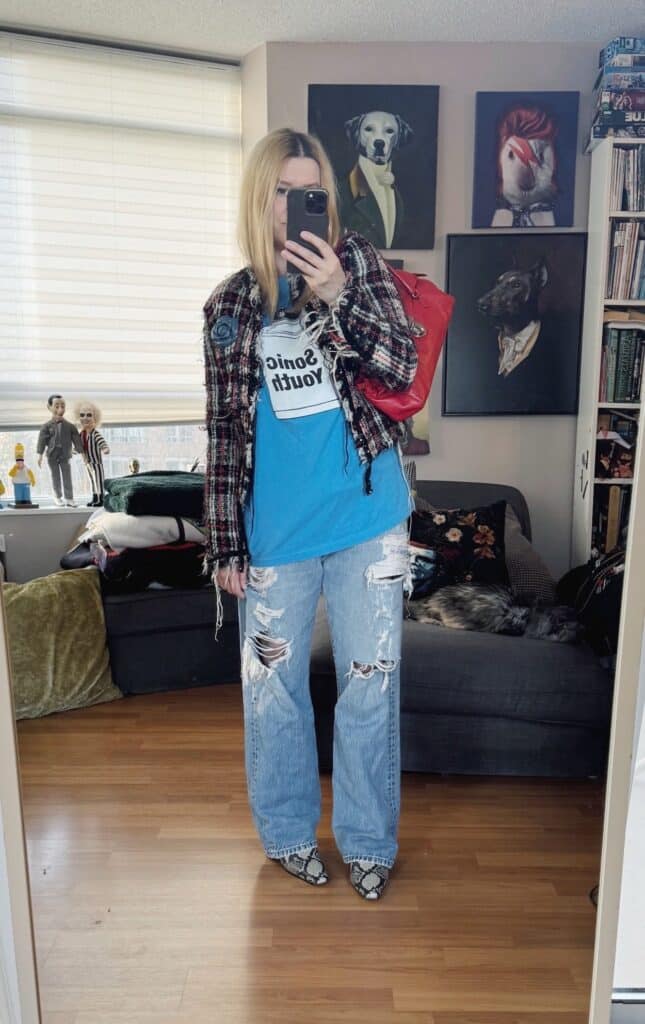 Sara of livelovesara is standing in front of a mirror taking a photo of her outfit. She is wearing a Sonic Youth t-shirt under a tweed jacket, distressed jeans, snake print boots, and a red bag.