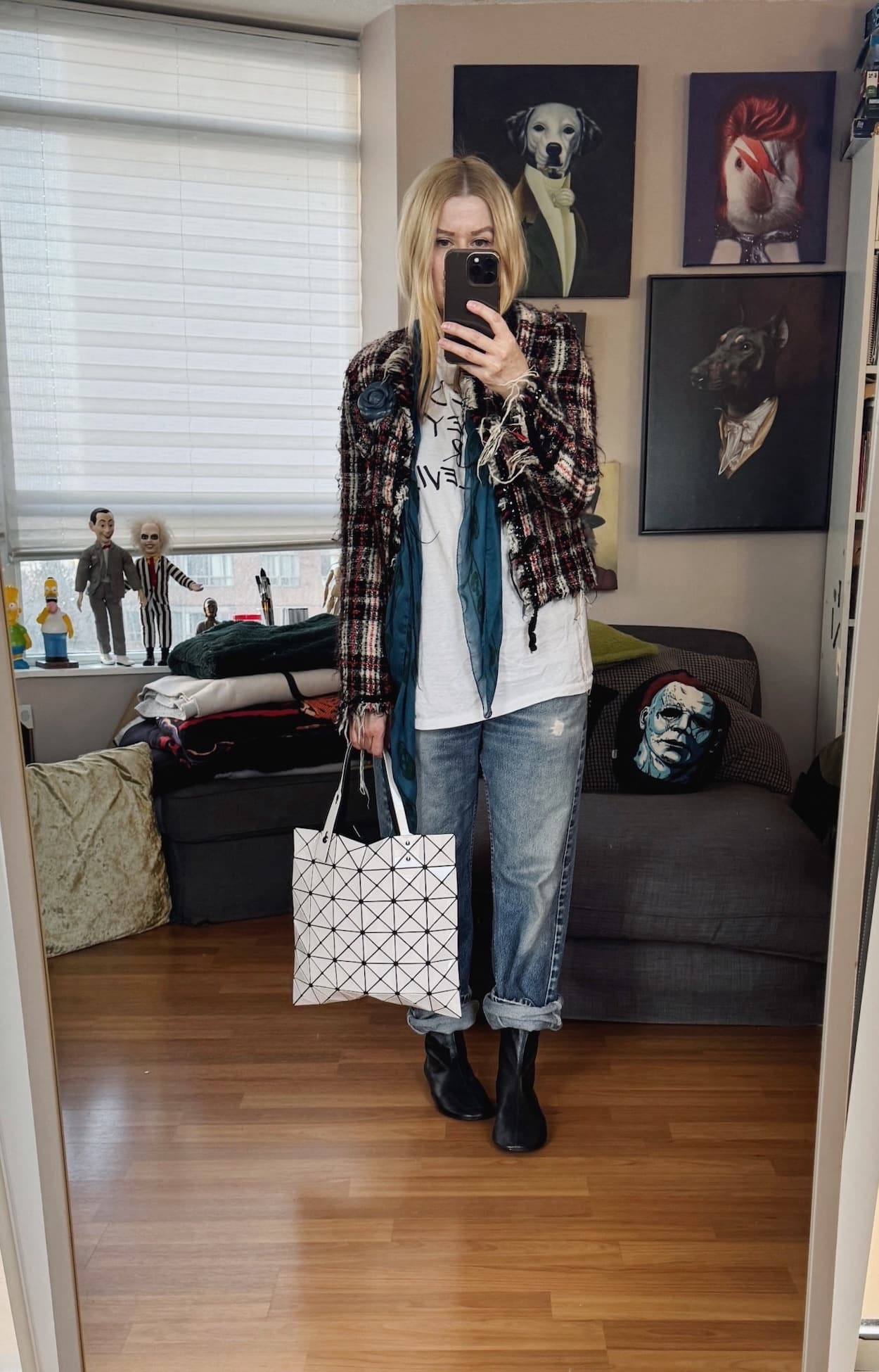 Sara of livelovesara is standing in front of a mirror taking a photo of her outfit. She is wearing a white t-shirt under a tweed jacket with a flower brooch, vintage Levis, and Alexander McQueen Skull, black boots, and an Issey Miyake Bao bao bag.
