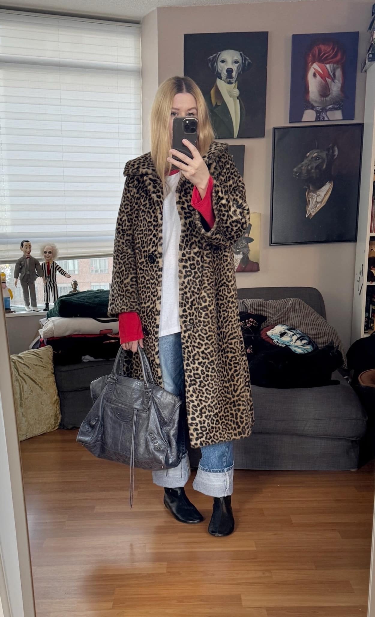 Sara of livelovesara is standing in front of a mirror taking a photo of her outfit. She is wearing a white baseball shirt with red sleeves, cuffed, vintage Levi's 517s, with a vintage animal print coat, black, flat boots, and a grey Balenciaga bag.