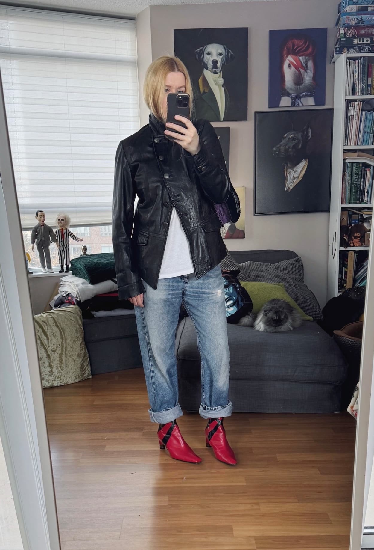 Sara of livelovesara is standing in front of a mirror taking a photo of her outfit. She is wearing a white tee under a vintage leather jacket, vintage Levi's cuffed over red vintage boots, and a purple snake print bag.