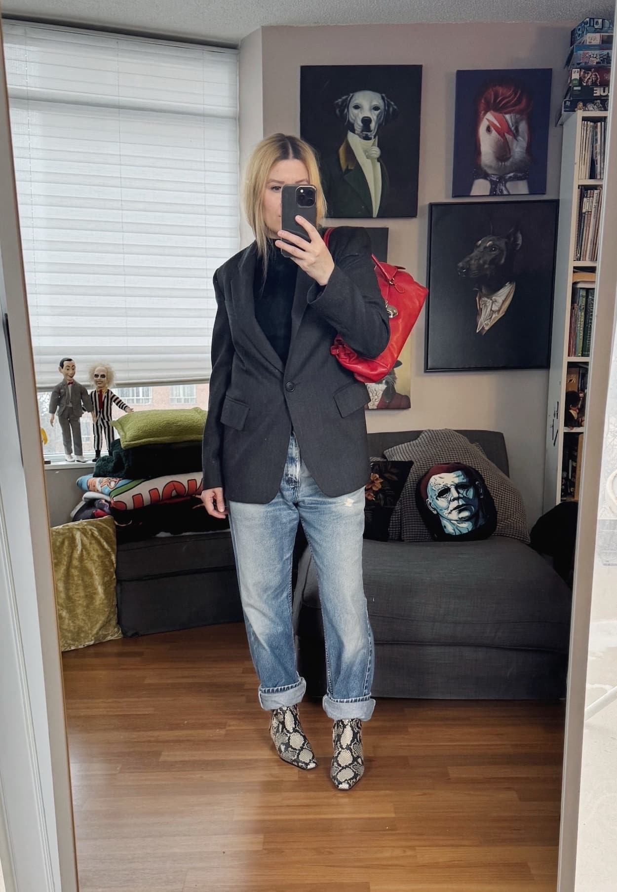 Sara of livelovesara is standing in front of a mirror taking a photo of her outfit. She is wearing a black turtleneck under a grey blazer, vintage Levi's, snake print boots, and a red Prada shoulder bag.