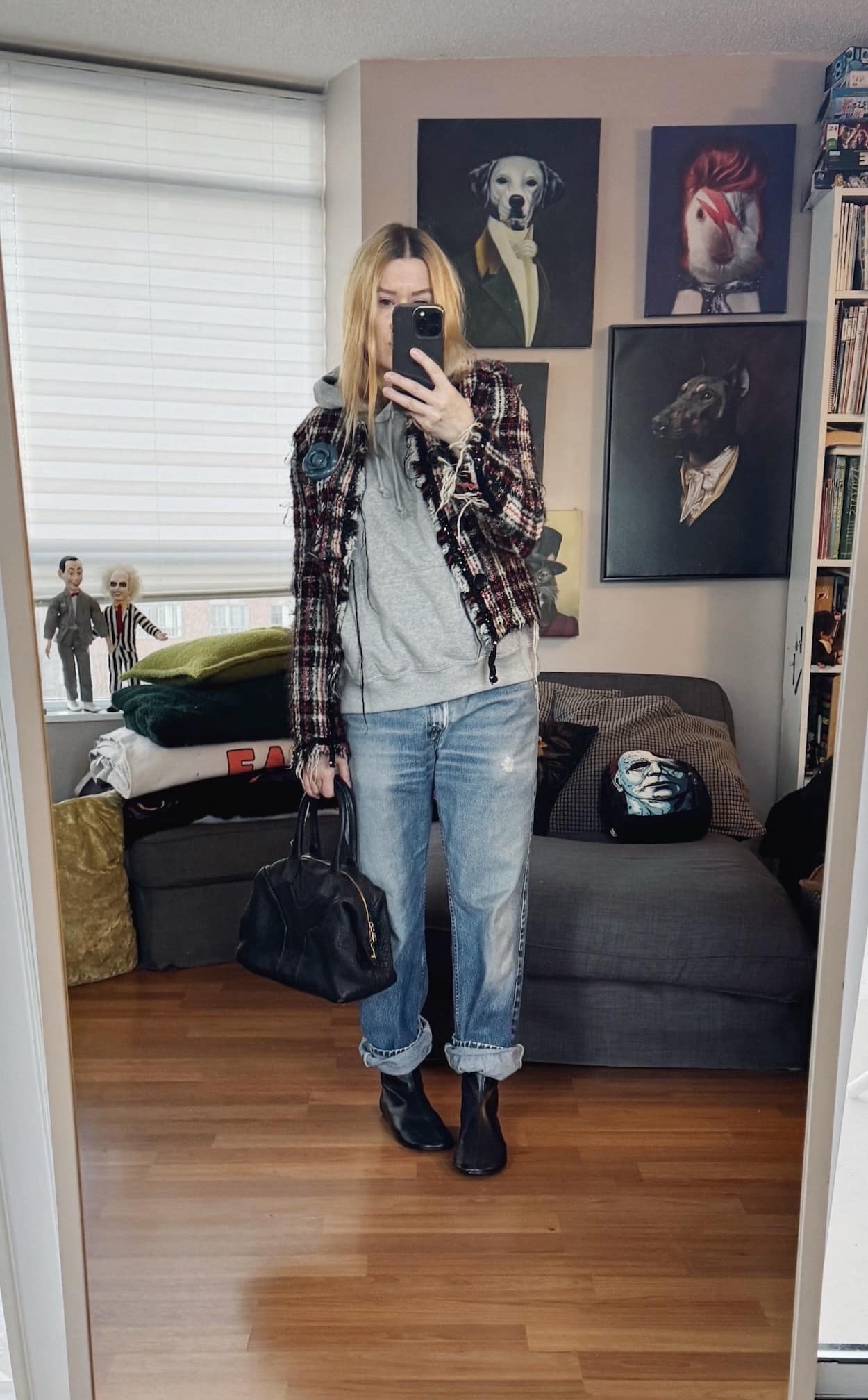 Sara of livelovesara is standing in front of a mirror taking a photo of her outfit. She is wearing a grey sleeveless hoodie under a tweed jacket with a blue flower brooch. Vintage Levi's, black flats boots, and a black YSL Easy bag.