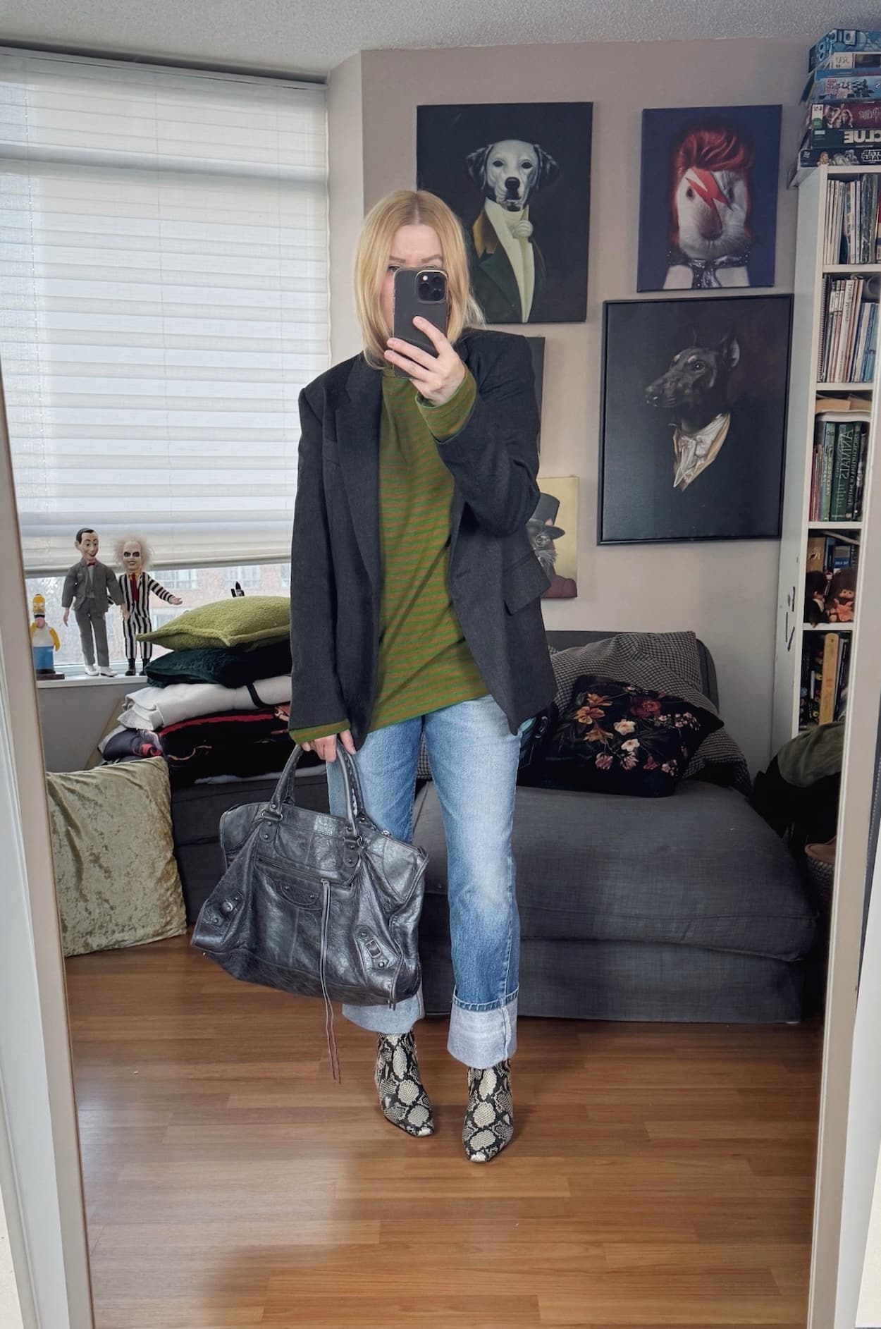 Sara of livelovesara is standing in front of a mirror taking a photo of her outfit. She is wearing a grenn and brown striped long sleeve under a grey blazer, vintage Levi's 517, snake print boots, and a grey Balenciaga city big.