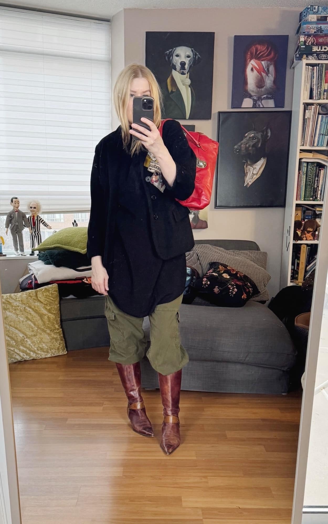 Sara of livelovesara is standing in front of a mirror taking a photo of her outfit. She is wearing a black sleeveless tunic under a black vintage blazer, green cargo pants tucked into calf height, pointy toe vintage boots in a reddish brown, and a red Prada Y2K bag.