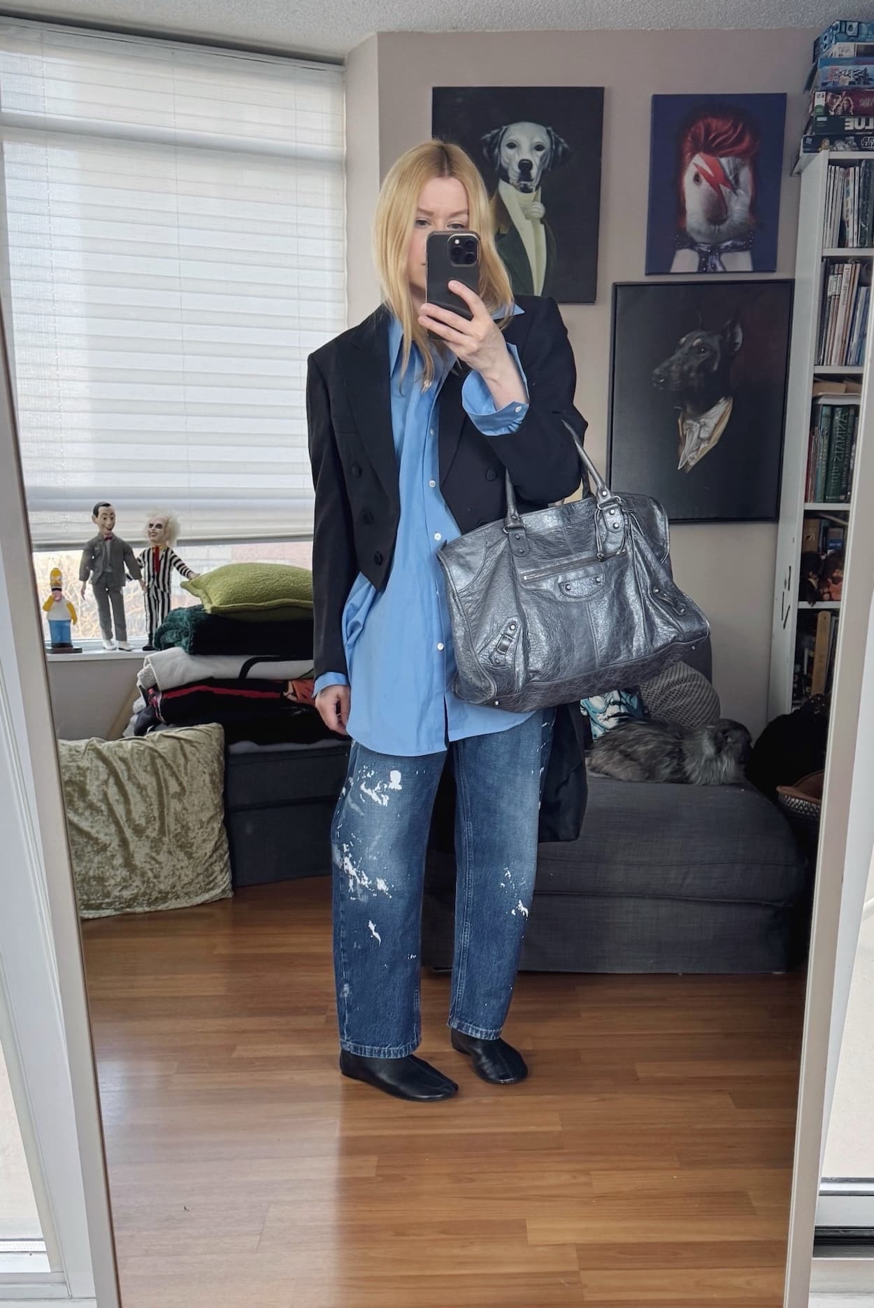 Sara of livelovesara is standing in front of a mirror taking a photo of her outfit. She is wearing a blue button up with paint splattered jeans, a vintage tailcoat, black flat boots, and a grey Balenciaga work bag.
