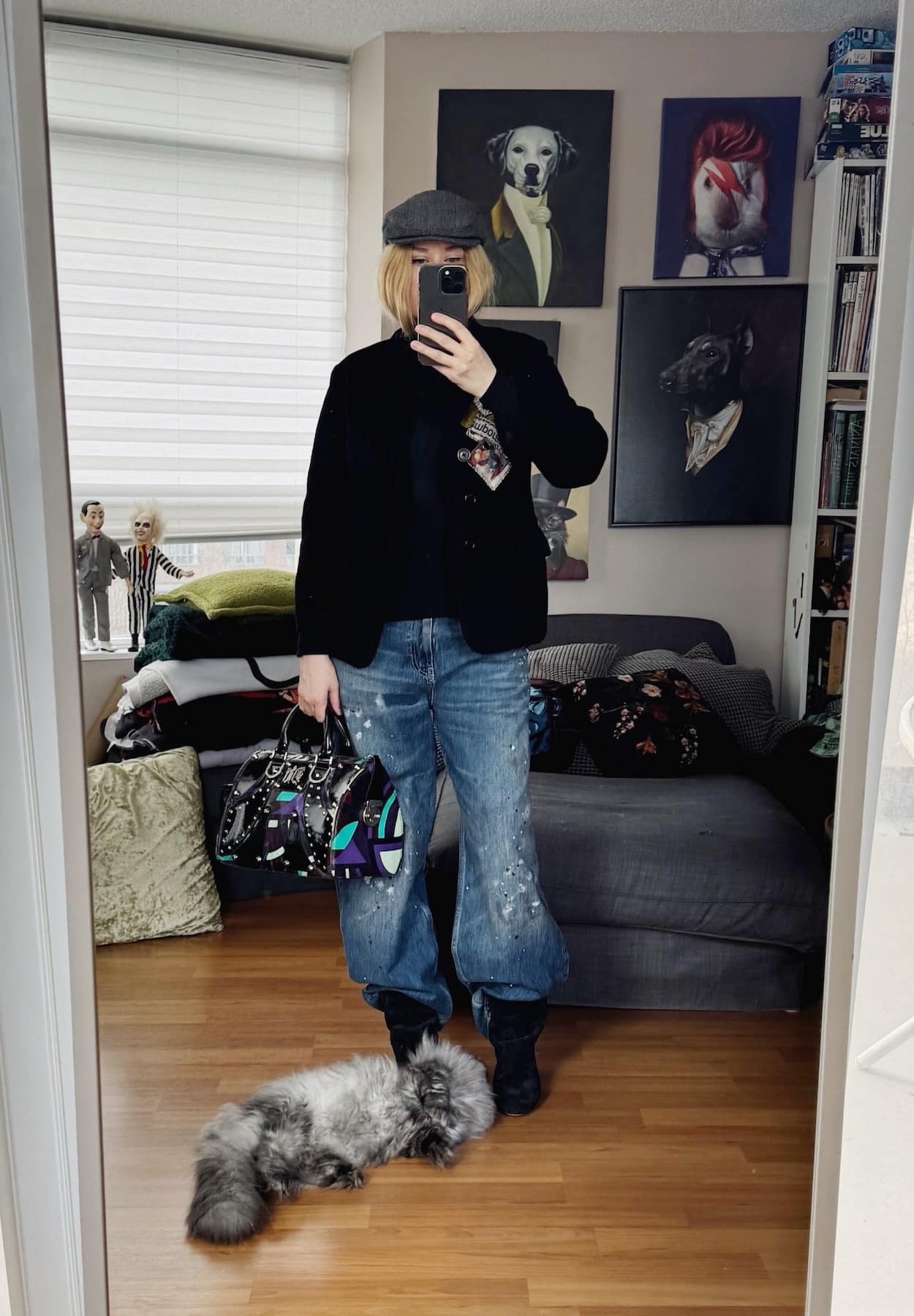 Sara of livelovesara is standing in front of a mirror taking a photo of her outfit. She is wearing a black turtleneck under a vintage Yohji Yamamoto blazer, paint splatter jeans tucked into black slouchy boots, a grey herringbone driving cap, and a Versace bag.