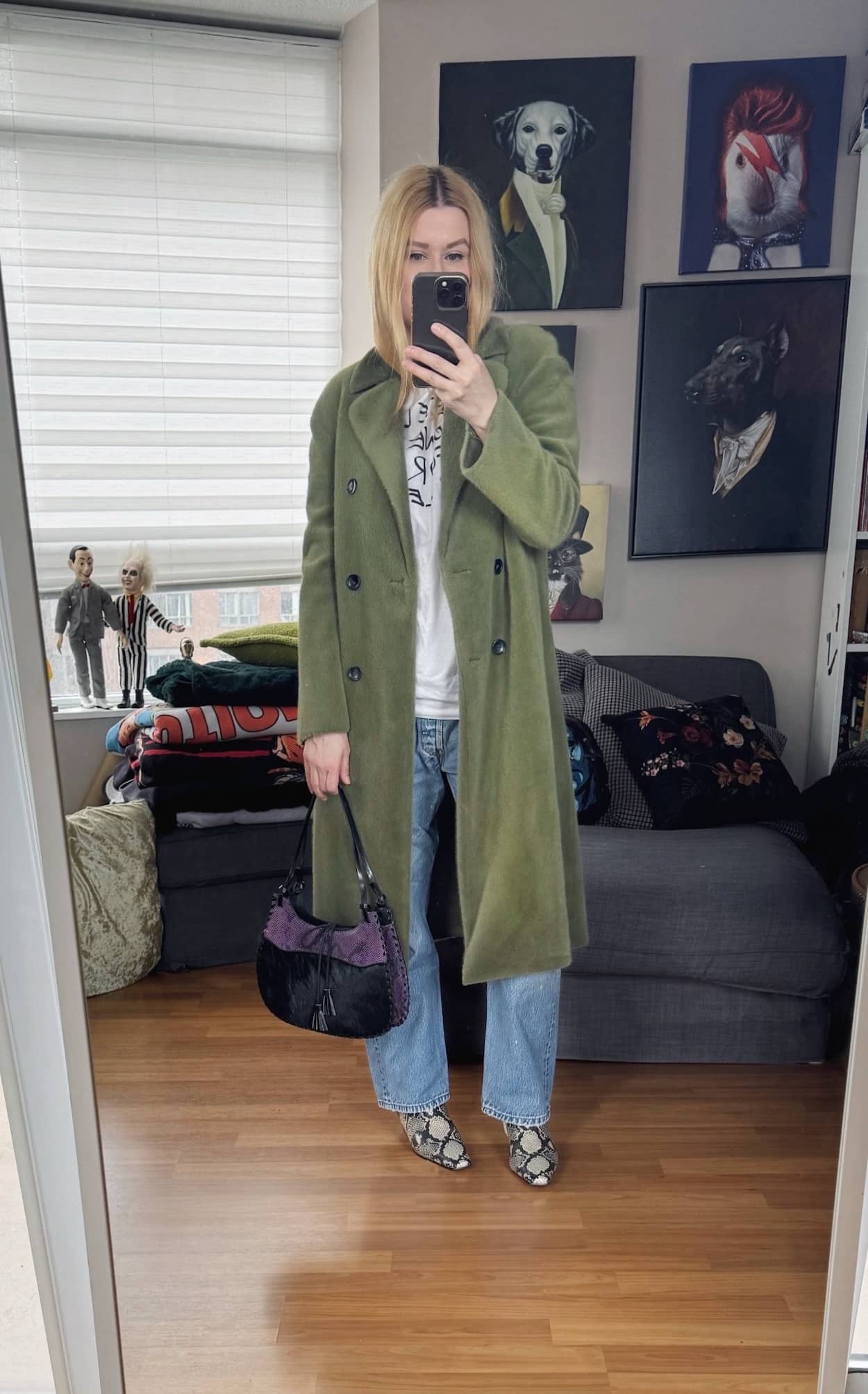 Sara of livelovesara is standing in front of a mirror taking a photo of her outfit. She is wearing a white vintage tee with "need money fro vintage Levis" on the front, vintage Levis, a green faux fur coat, snake print boots, and a purple and black vintage snake print bag.