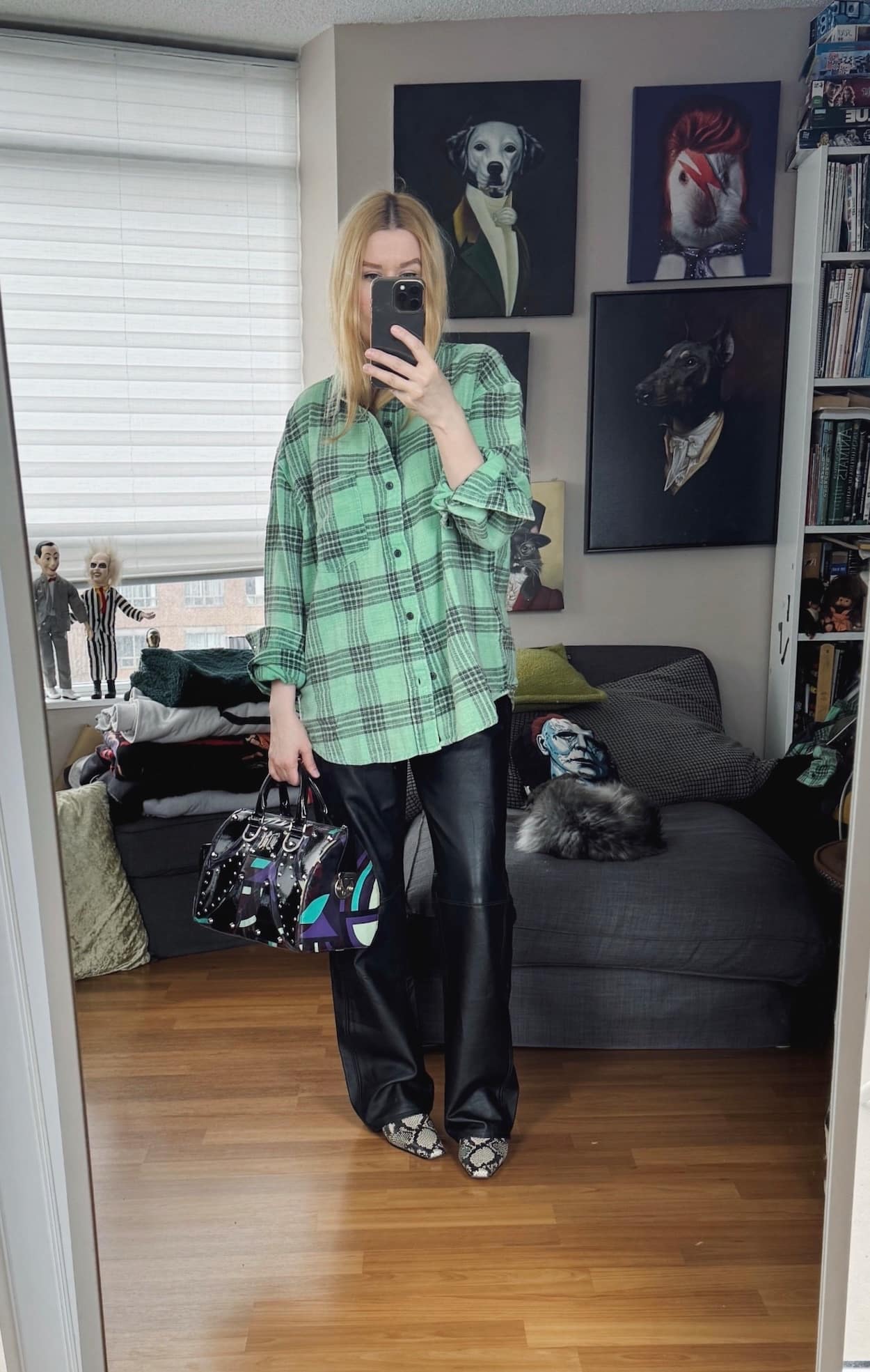 Sara of livelovesara is standing in front of a mirror taking a photo of her outfit. She is wearing a light green plaid shirt with vintage black leather pants, snake print boots, and a Versace bag.