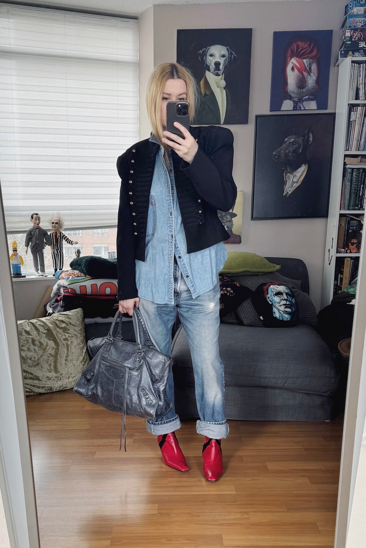 Sara of livelovesara is standing in front of a mirror taking a photo of her outfit. She is wearing a vintage levis denim shirt under a Napoleon jacket, vintsge Levis jeans, red boots, and a grey Balenciaga bag.