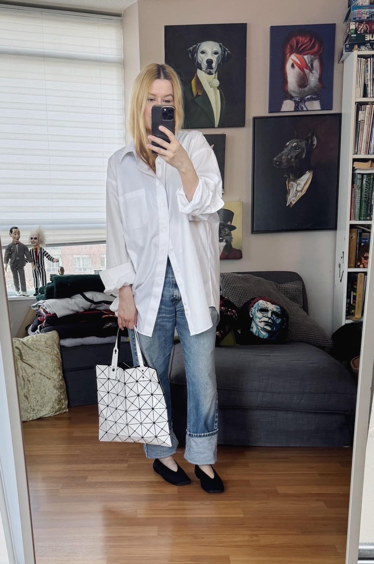 Sara of livelovesara is standing in front of a mirror taking a photo of her outfit. She is wearing an oversized men's white button up with vintage Levis that are cuffed, black pony hair flats, and a white Issey Miyake Bao Bao bag.