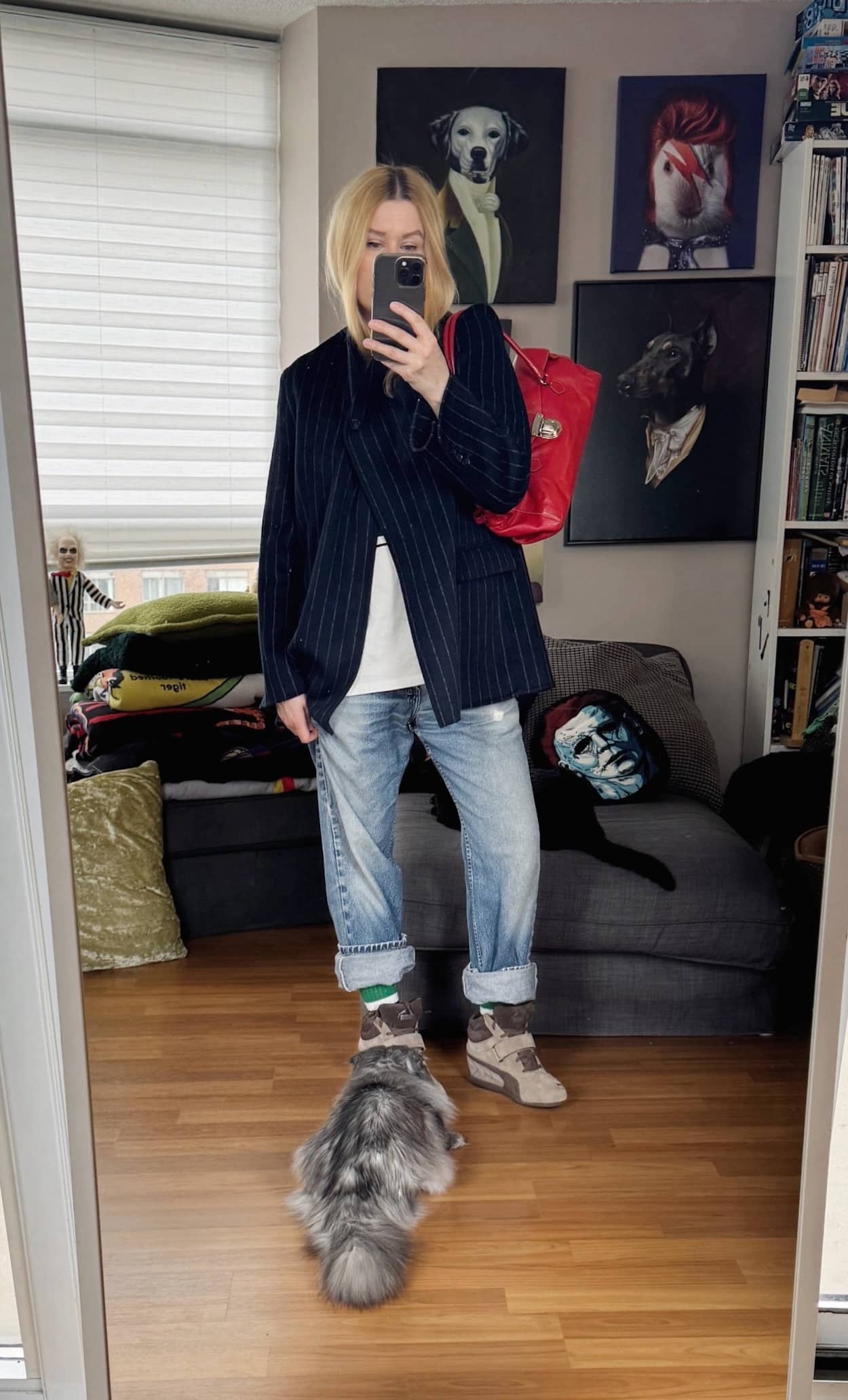 Sara of livelovesara is standing in front of a mirror taking a photo of her outfit. She is wearing a Vision Streetwear tee under a navy blue blazer, vintage levis, a red prada bag, and brown wedge sneakers.